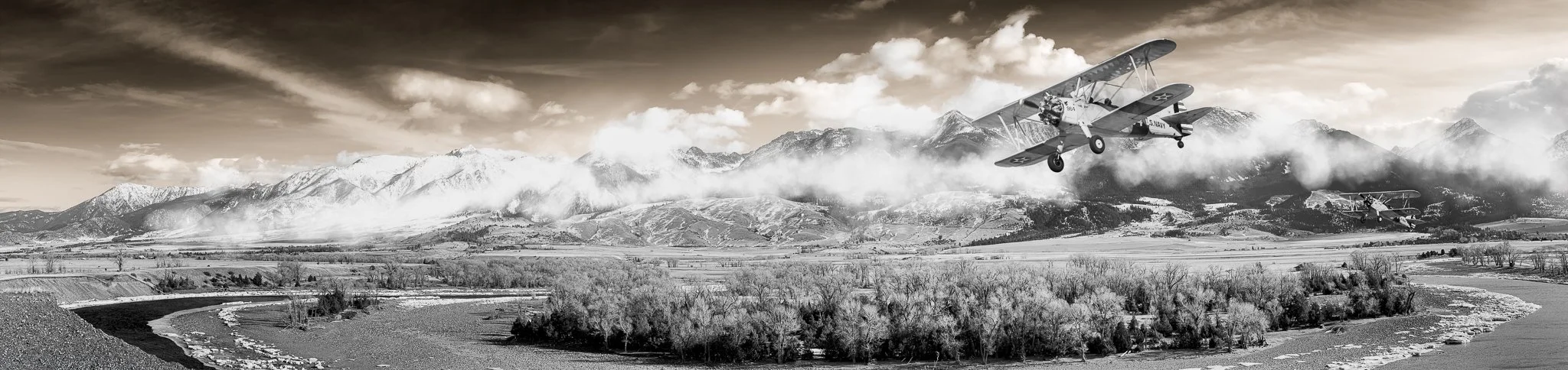 Black-and-white panoramic view of a biplane flying above Paradise Valley, Montana, with the Yellowstone River and mountains below.