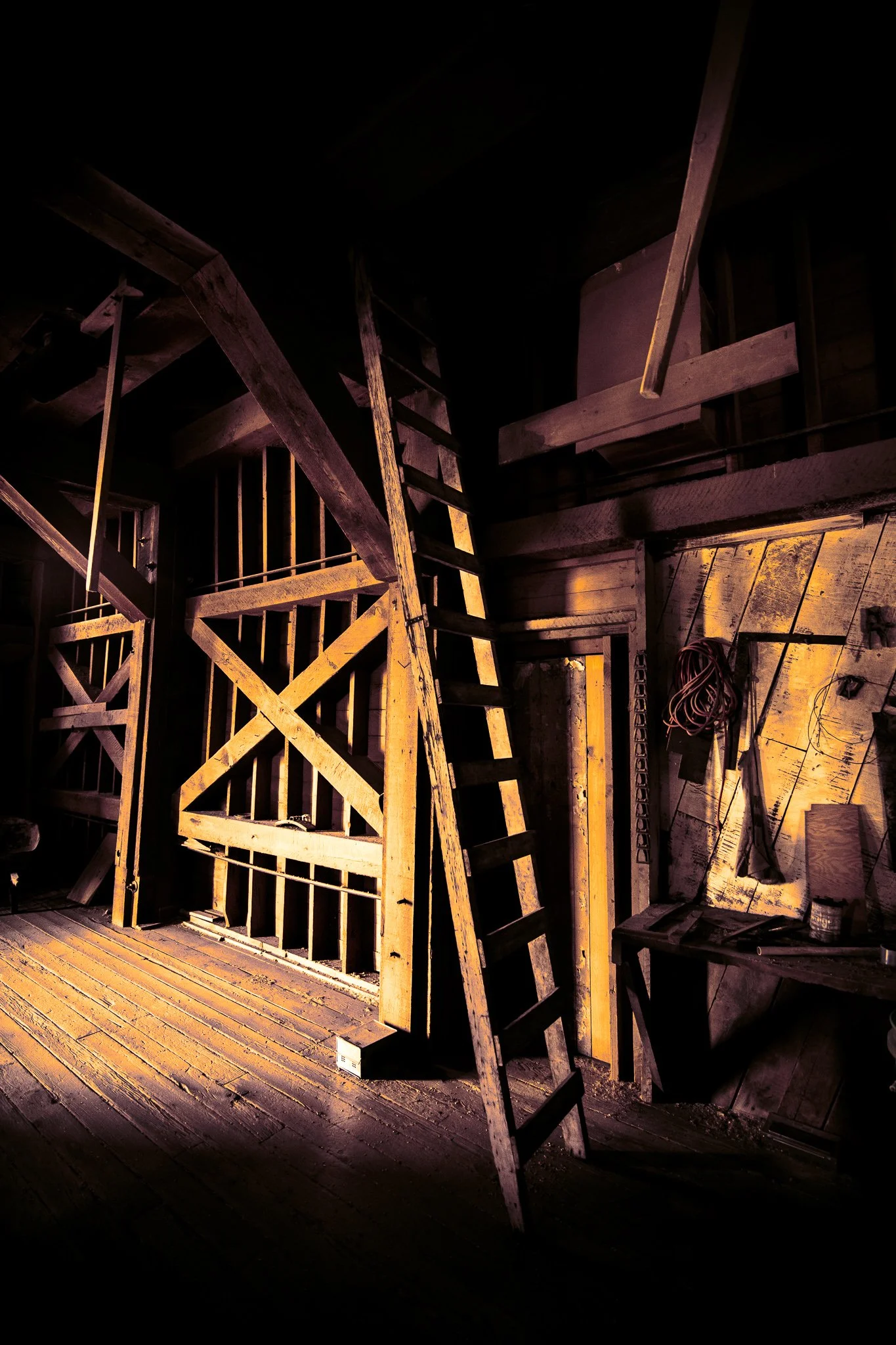 Interior of an old Montana barn with weathered wooden beams, aged boards, and a ladder illuminated by warm light.