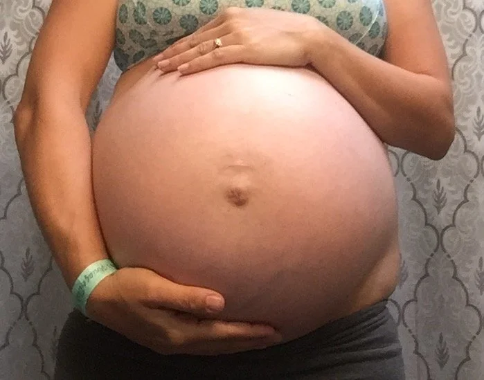 Very pregnant person with one hand above and one above their belly.