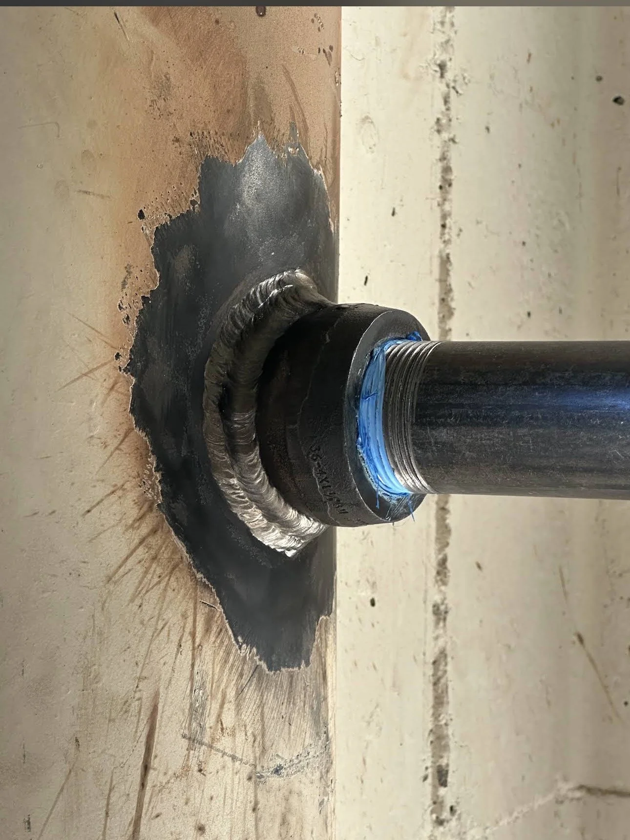 Close-up of a welded pipe fitting attached to a metal pipe, with visible welding seam and black sealant around the joint.