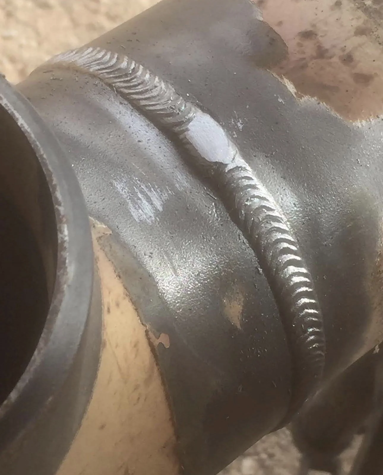 Close-up of a metallic weld joint on a large metal pipe with a visible bead of weld along the seam.