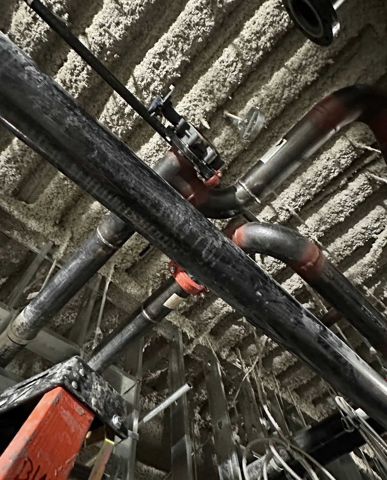 A ceiling with exposed pipes, valves, and insulation material.
