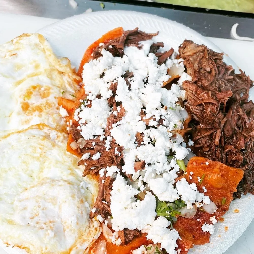 Plate of Mexican food with fried eggs, shredded beef, vegetables, and crumbled cheese.