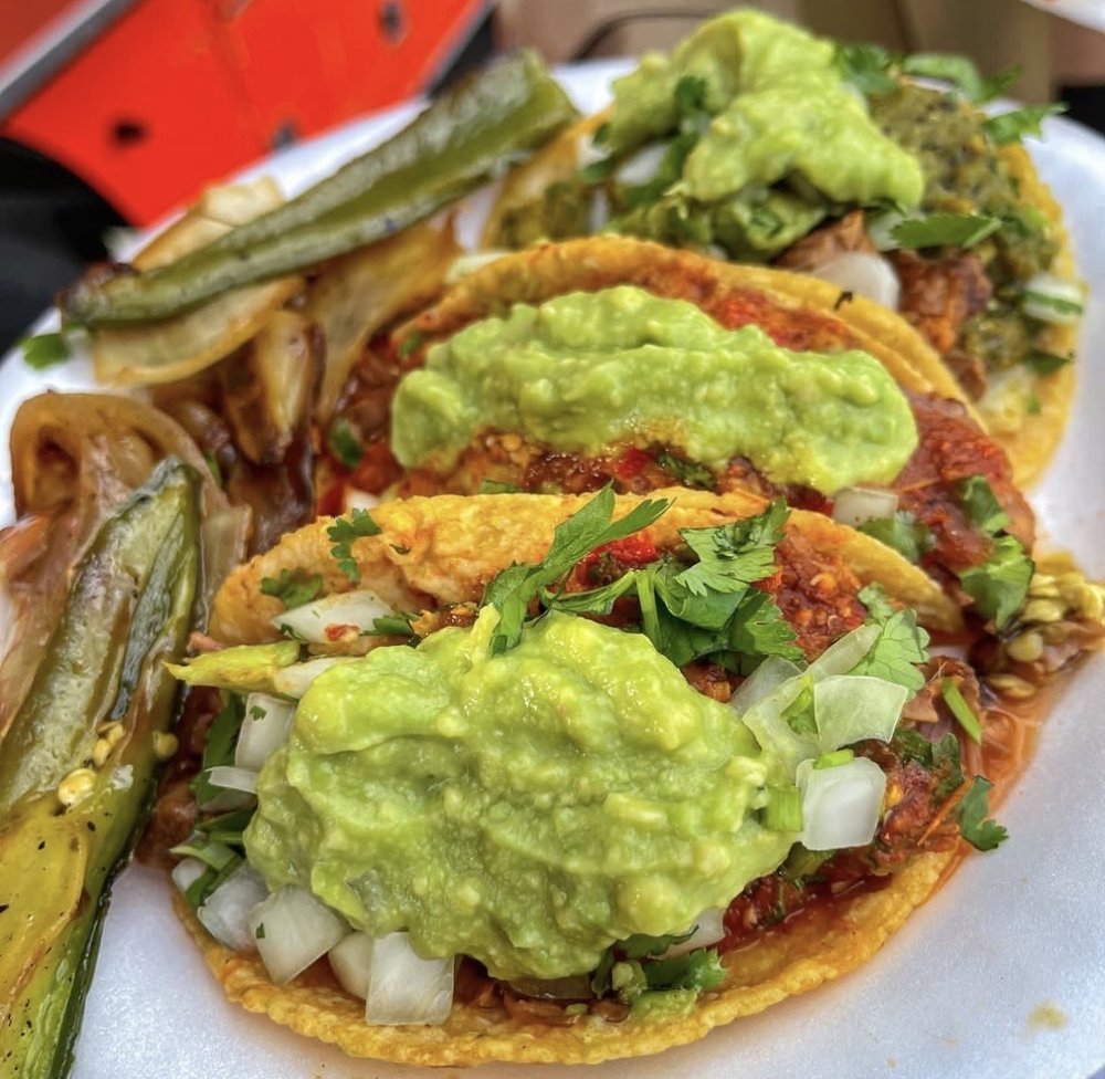 Three tacos with guacamole, chopped onions, cilantro, and meat, alongside grilled zucchini.