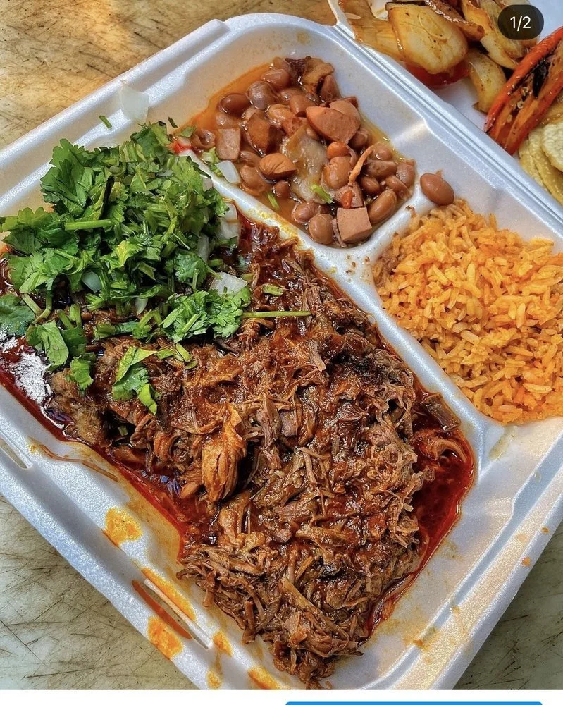 Barbecue pulled pork with chopped cilantro, a side of baked beans, Mexican rice, and roasted vegetables in a white foam takeout container.