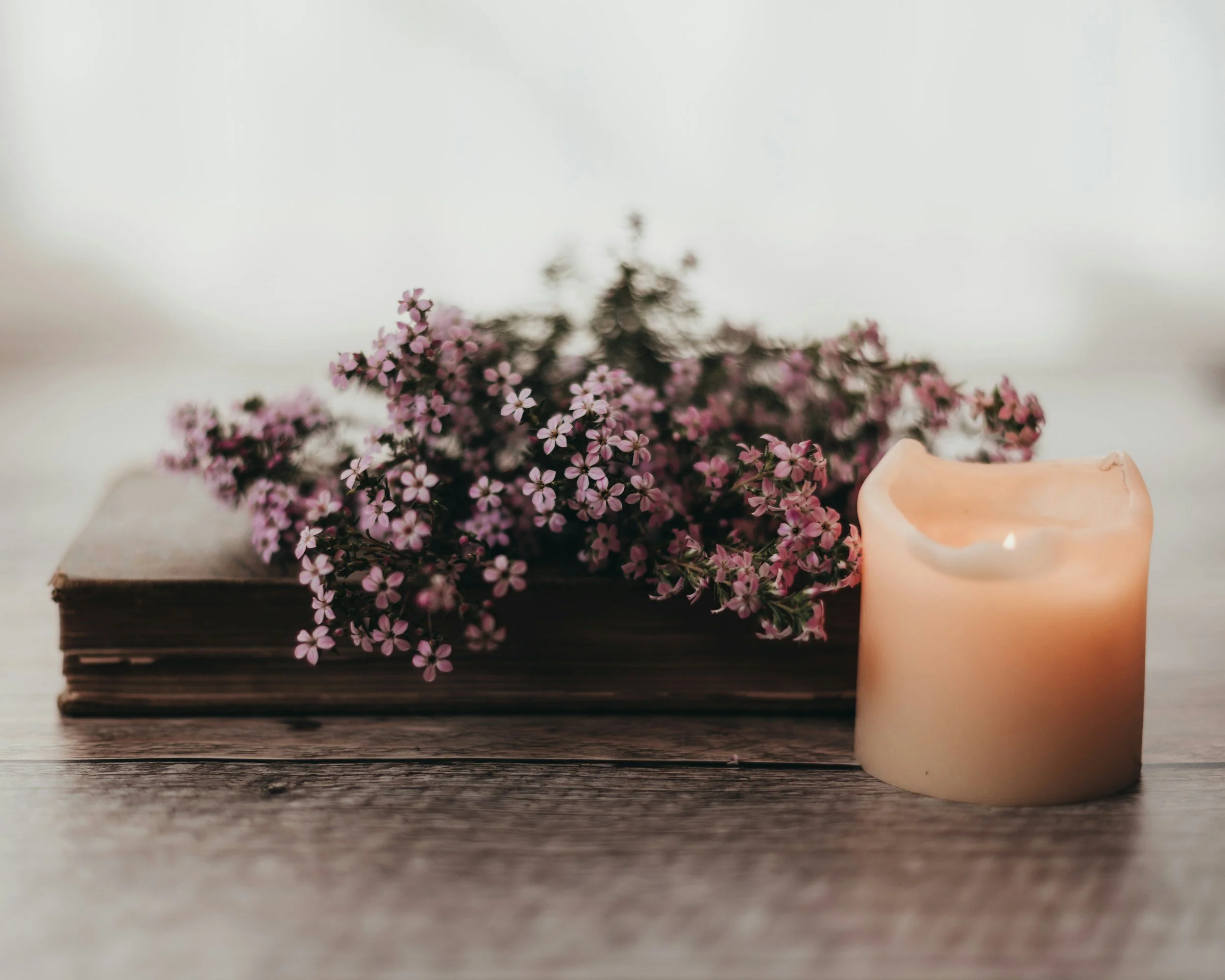 Warm, calming still life with candle, journal, and flowers.