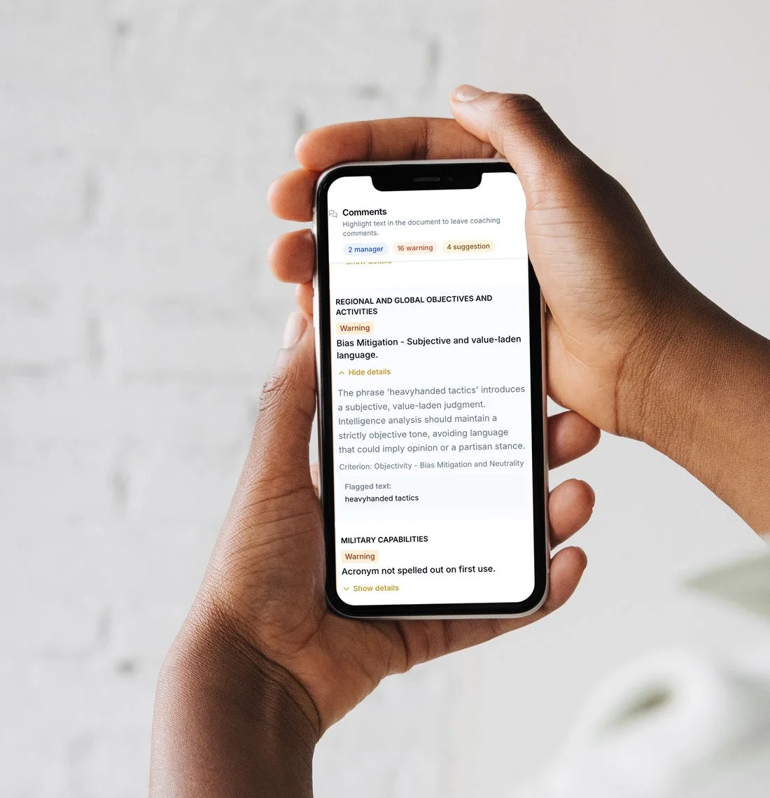 Second Set | Person holding a smartphone displaying a document with comments and warnings about bias mitigation and military capabilities