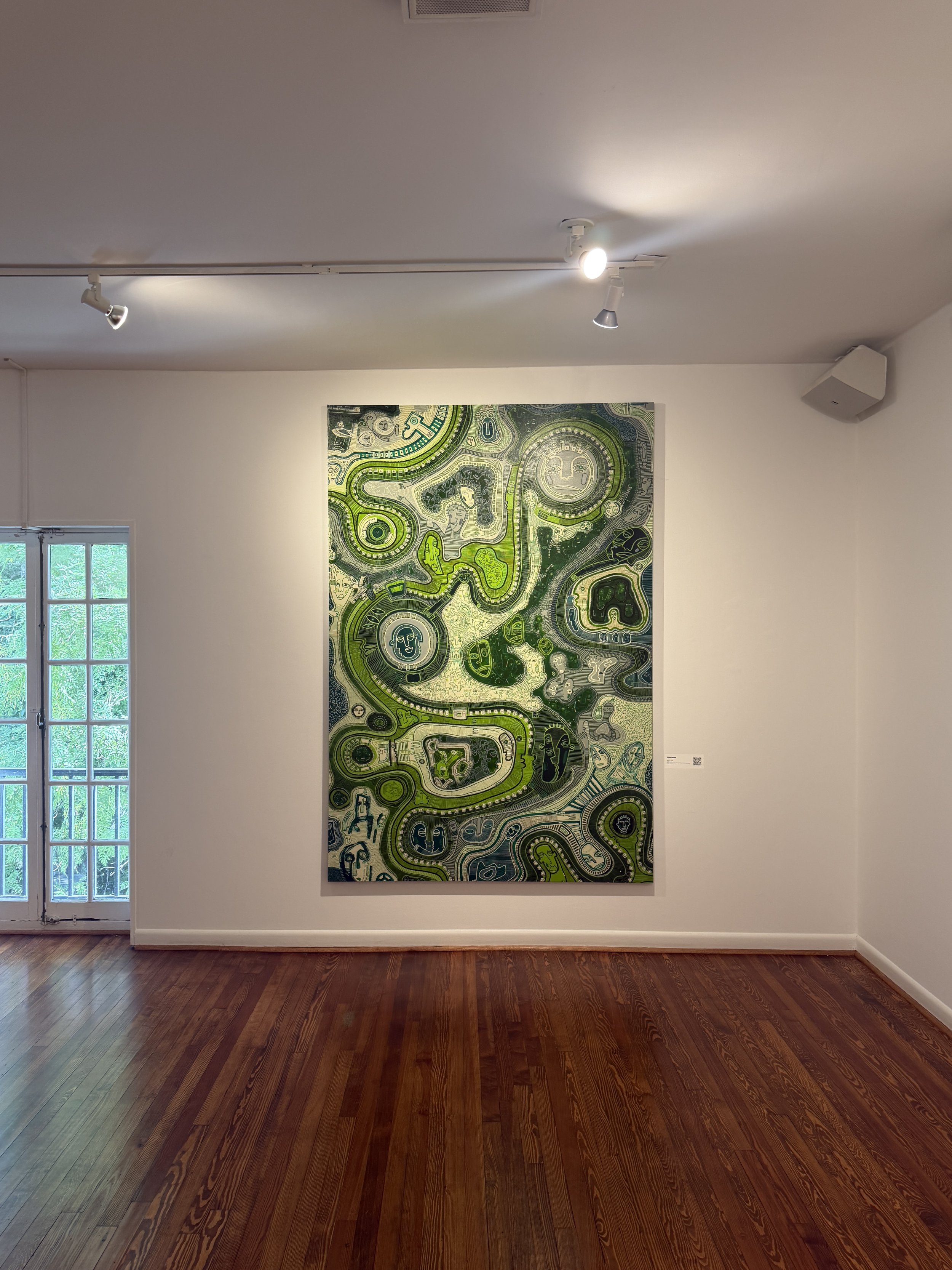 A large abstract painting with intricate green, black, and white patterns and faces, hanging on a white wall in an art gallery with wooden floors, next to a window and ceiling lights.