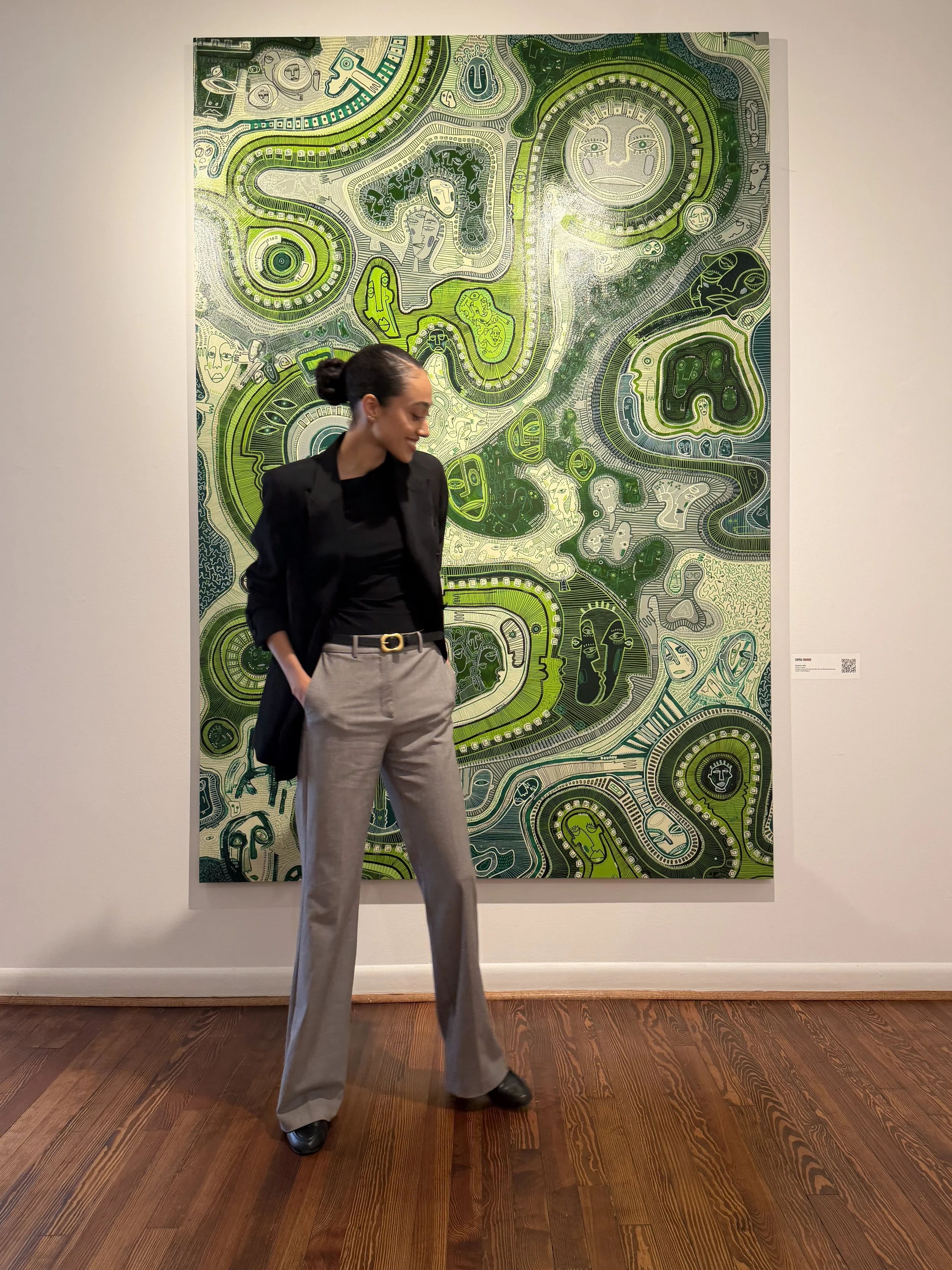 A woman stands in front of a colorful abstract artwork at a gallery, with her head slightly inclined and smiling.