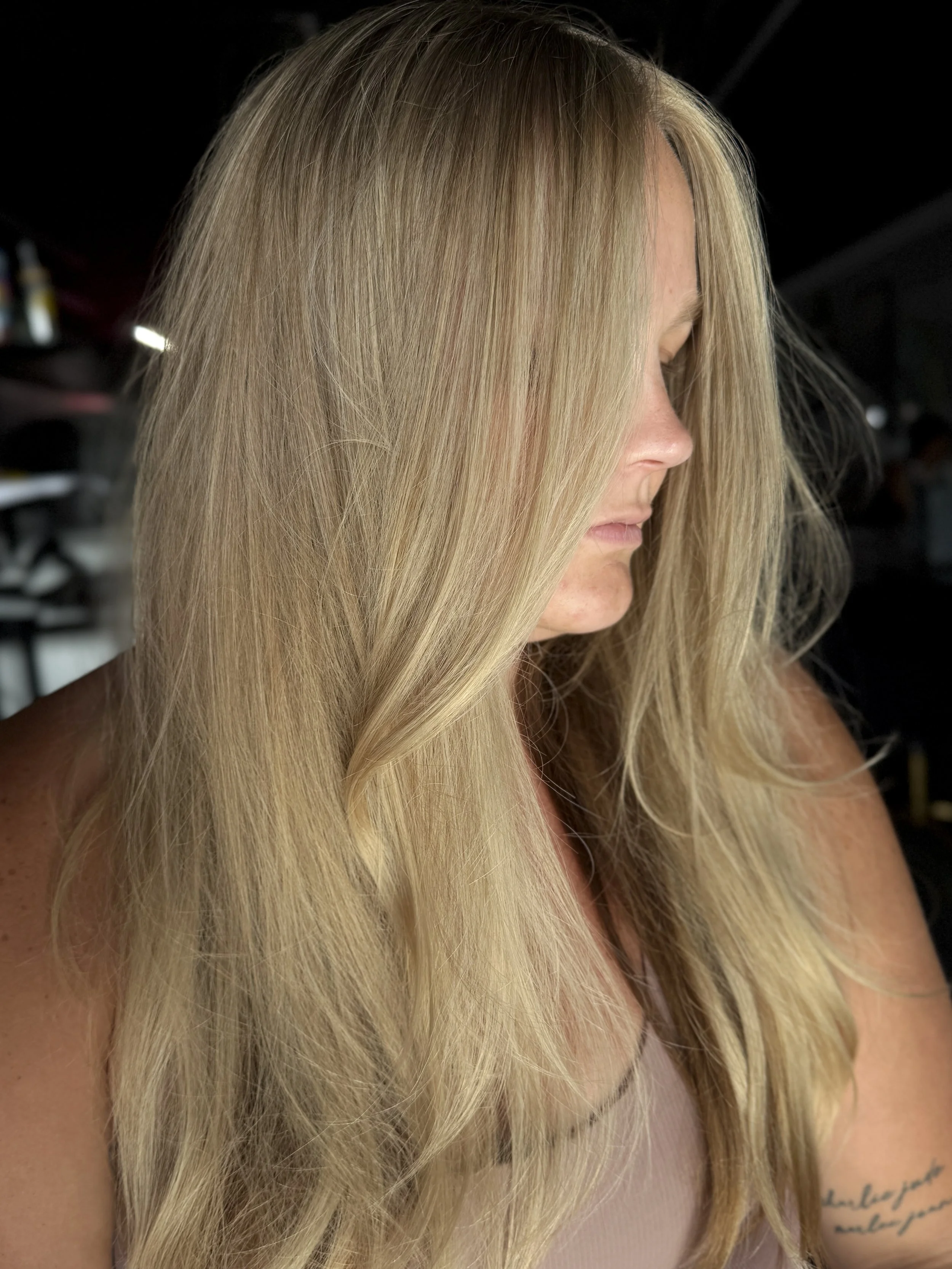 Close-up of a woman with long, wavy blonde hair, face turned to the side, in a low-light environment.