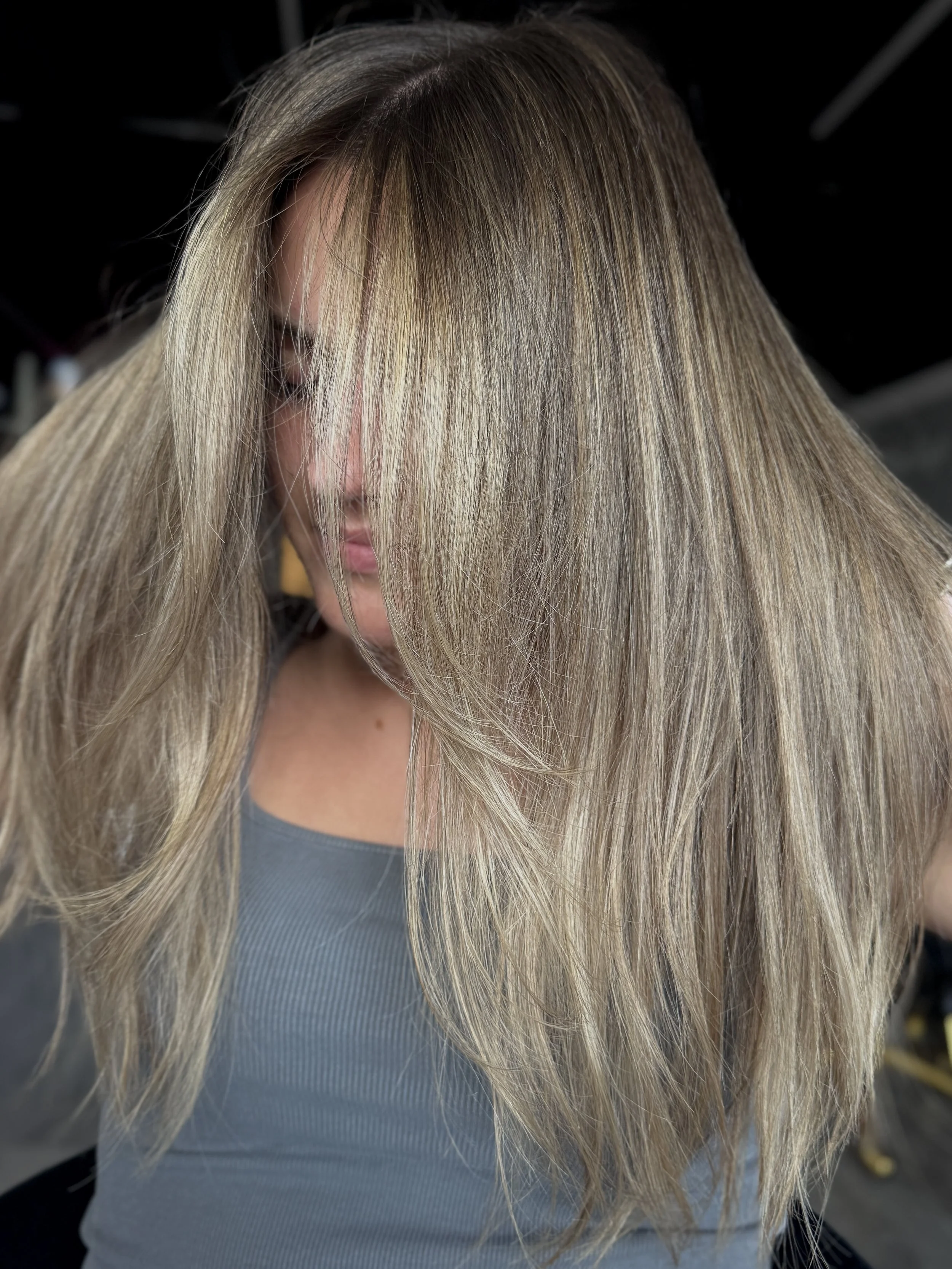 Close-up view of a woman's head with long, straight blonde hair covering her face, wearing a gray top.