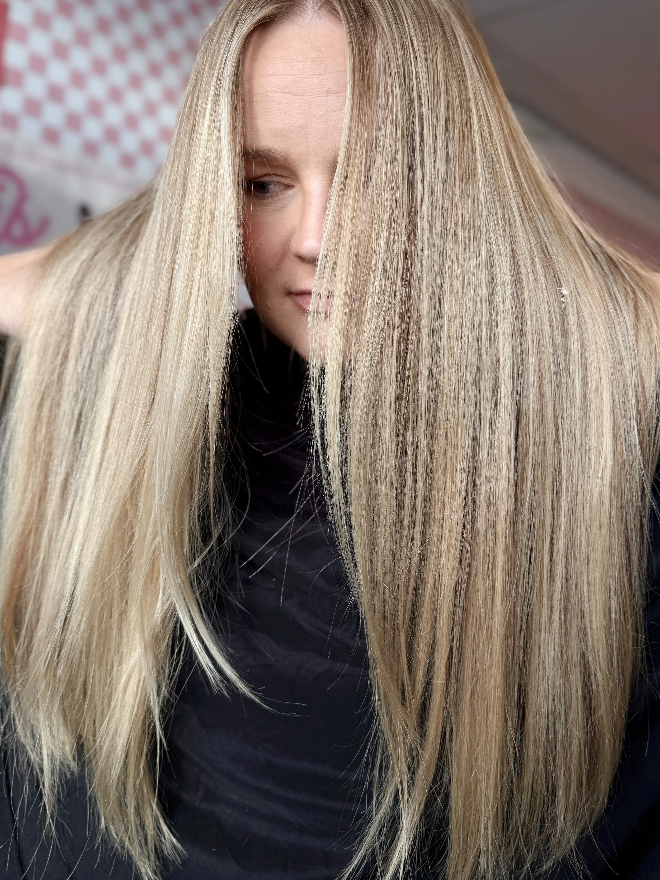 Close-up of a woman with long, straight blonde hair and a focused expression, partially covering her face with her hair.