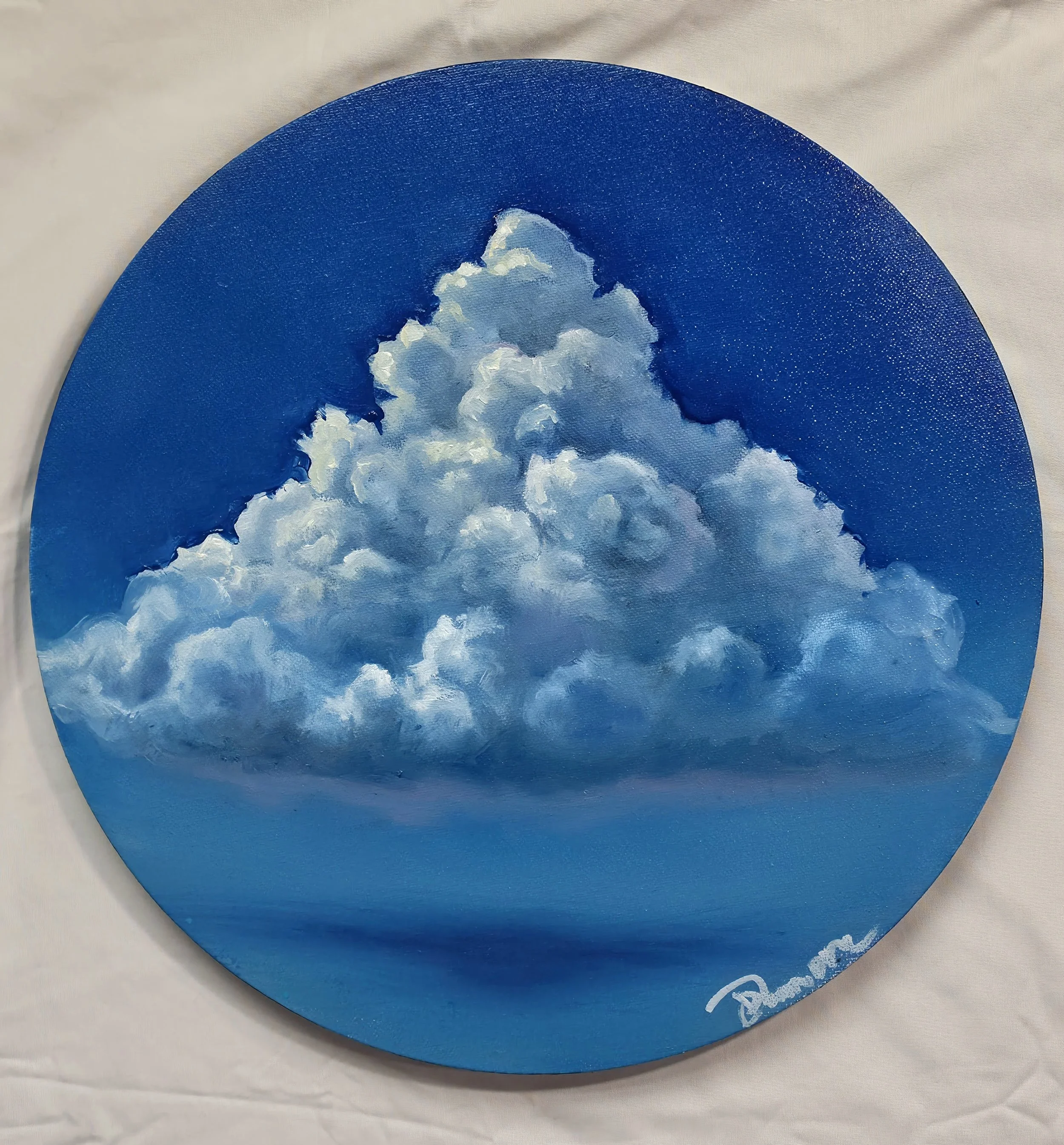 A painted circular wooden piece featuring a sky scene with fluffy clouds on a blue background.