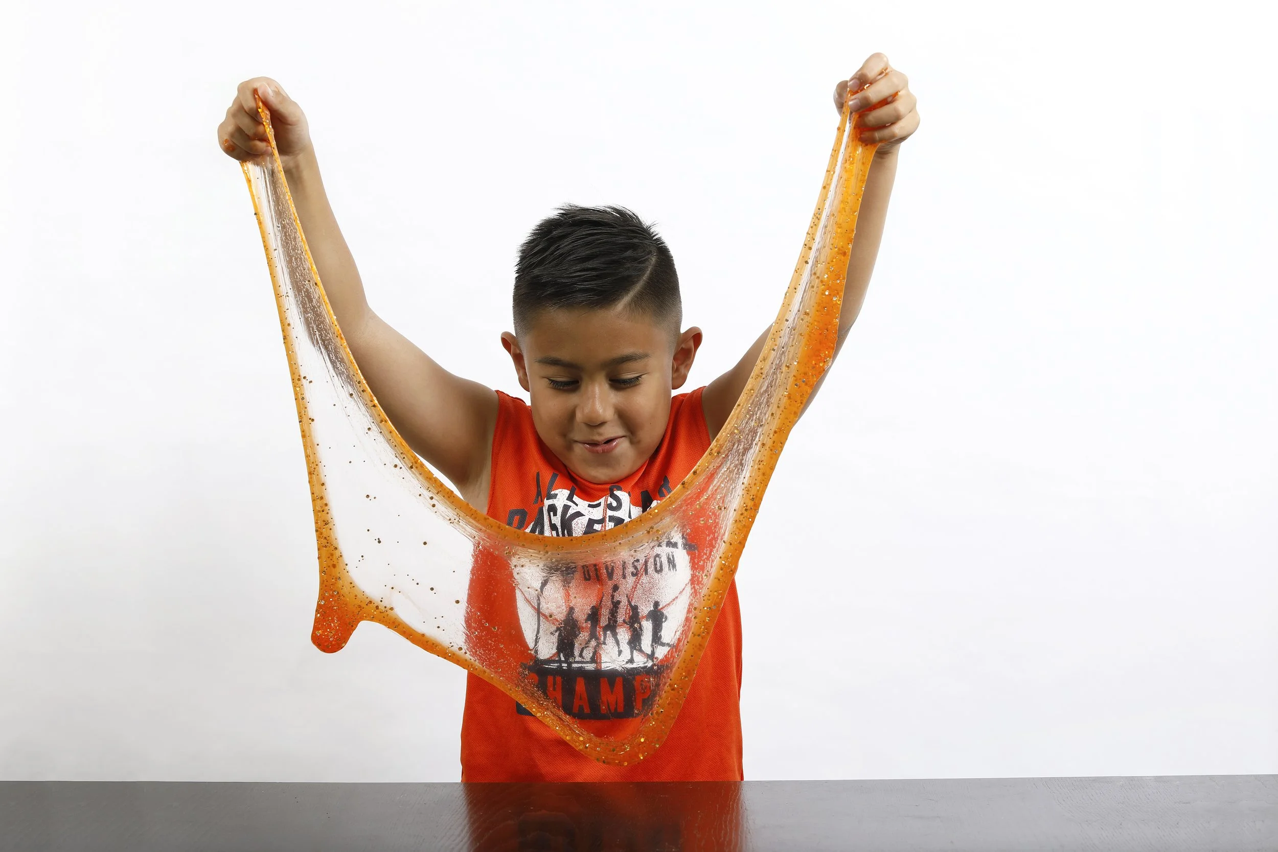 Boy stretching orange glitter slime between his hands during a Messy Play Slime Party.