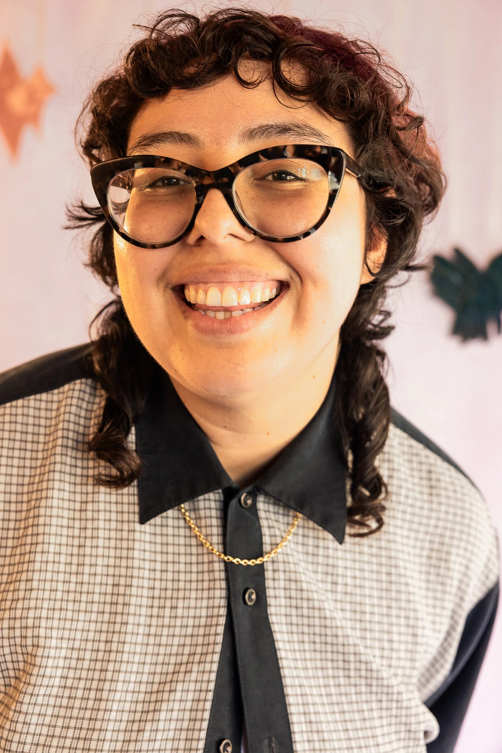 Messy Play team member with curly dark hair and tortoiseshell glasses wearing a plaid jacket and black collared shirt
