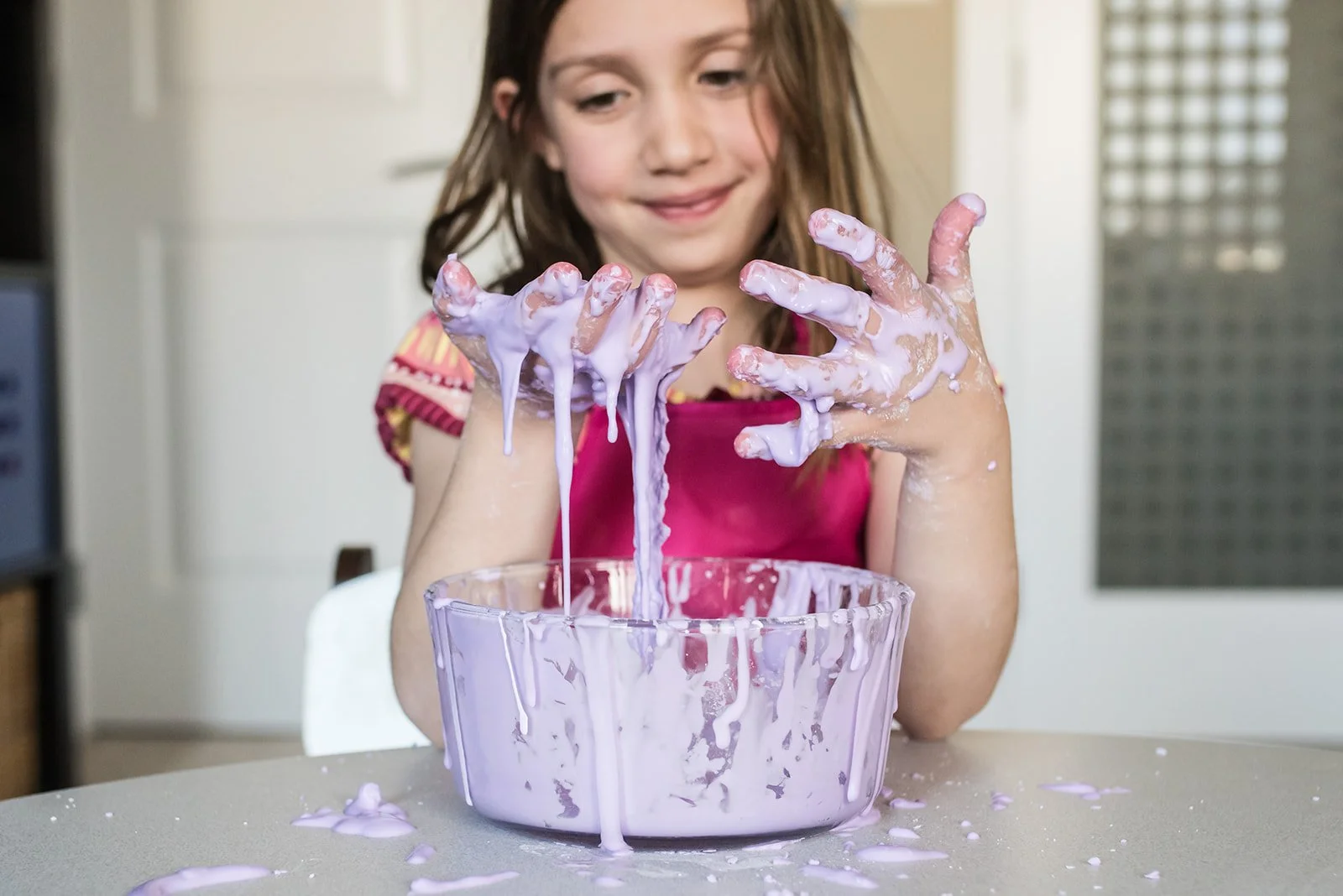 Smiling girl playing with purple slime in a bowl