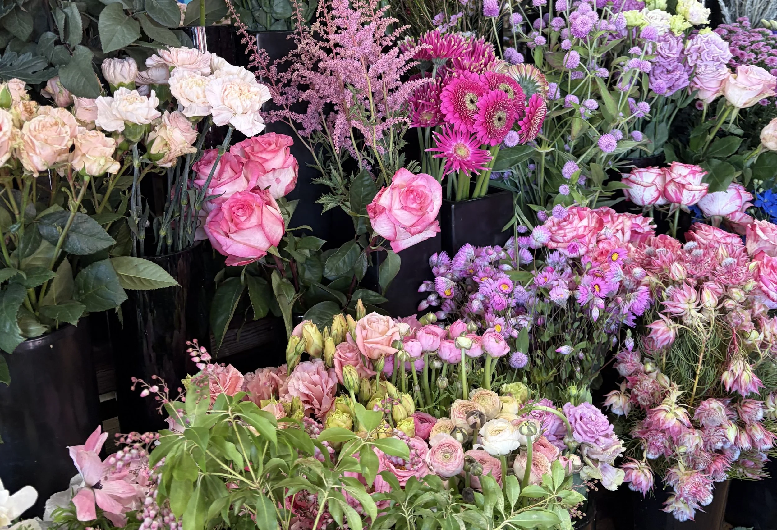 Various colorful flowers in a floral display, including pink roses, purple alliums, and pink daisies.