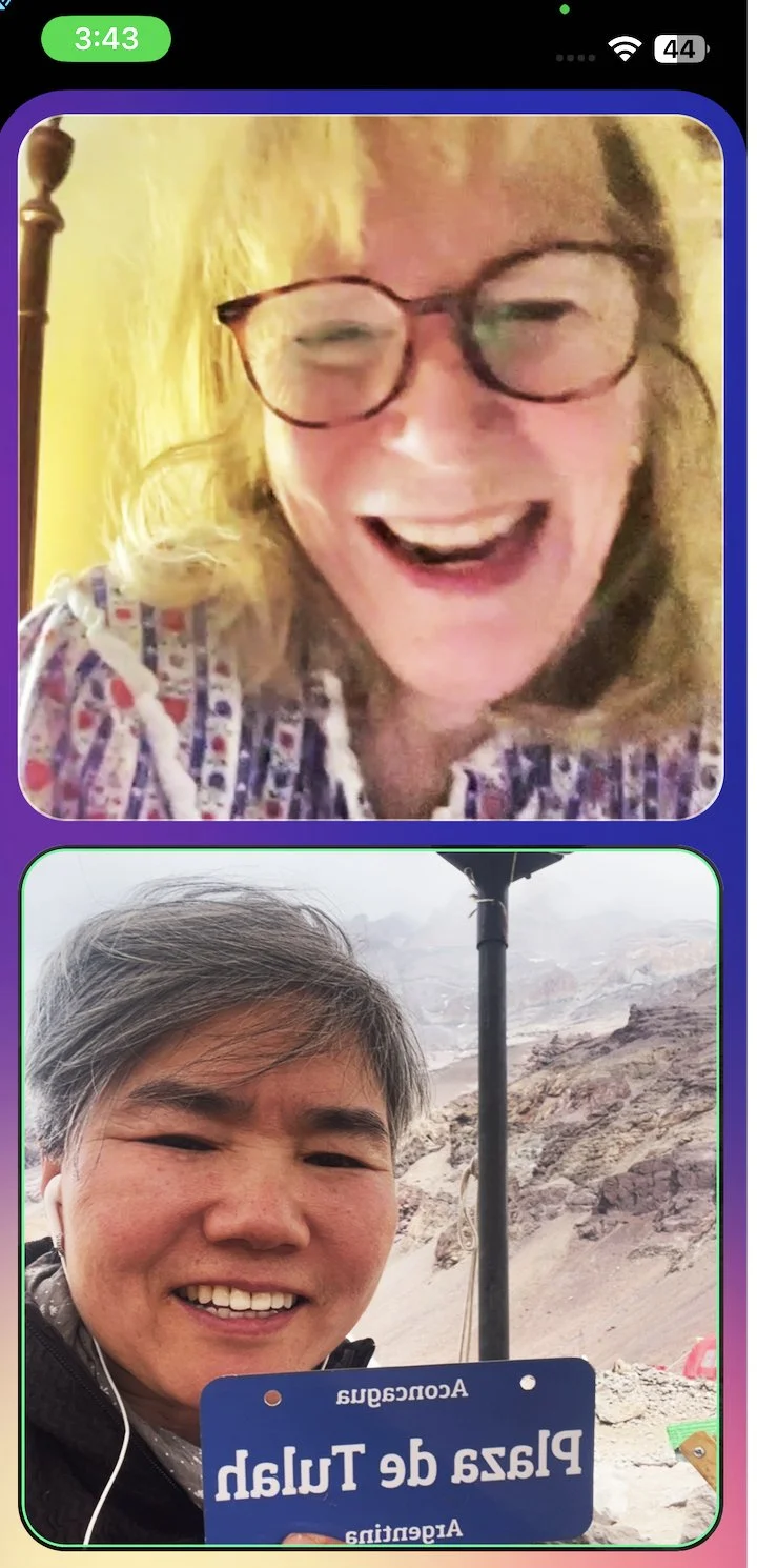 A woman with blonde hair and glasses smiling and a man with gray hair smiling, holding a blue sign that says "Plaza de Tula" in a desert landscape.