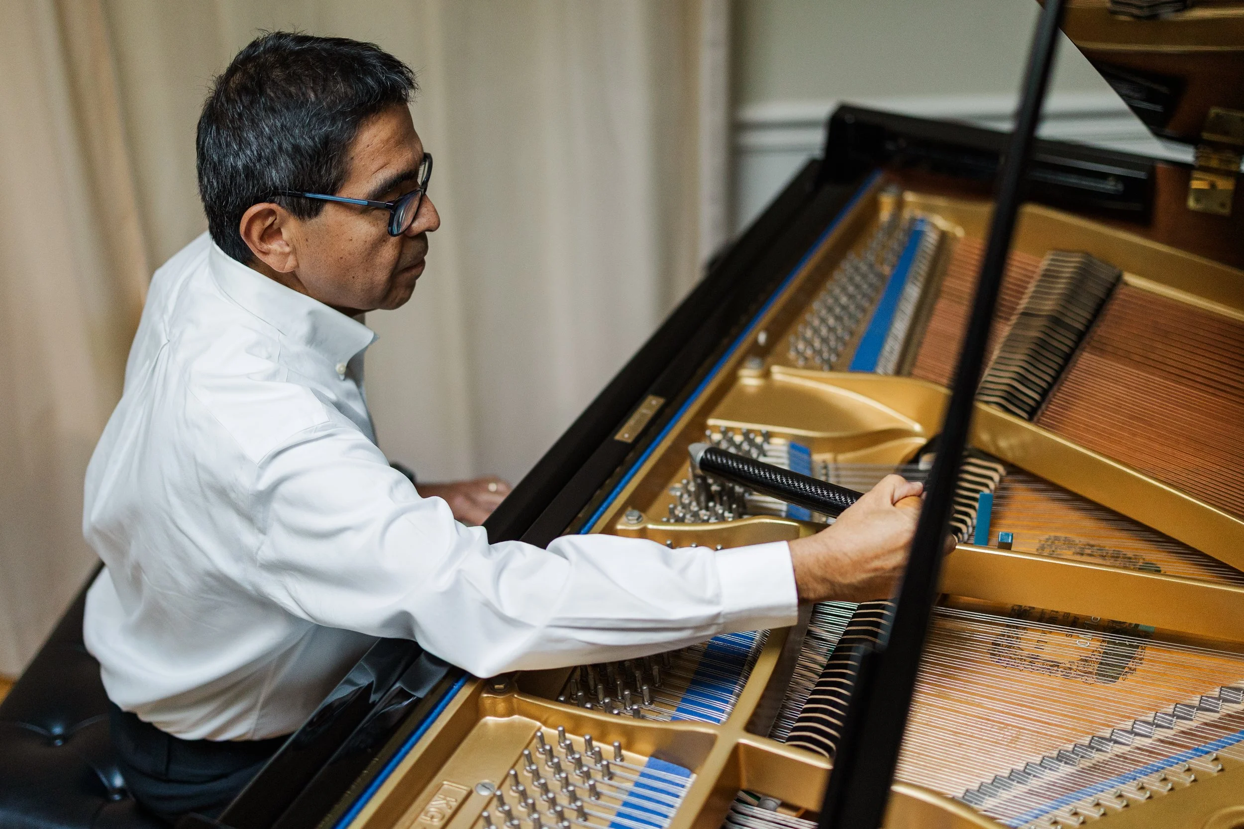 A man with glasses and a white shirt playing a grand piano.