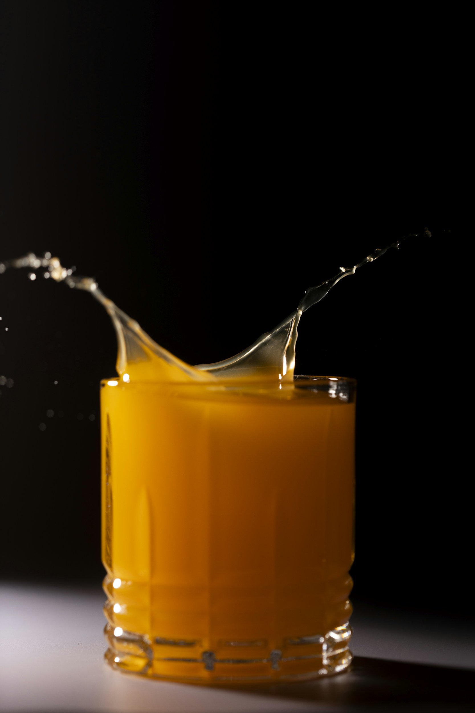 A glass of orange juice with a splash captured in motion against a black background.