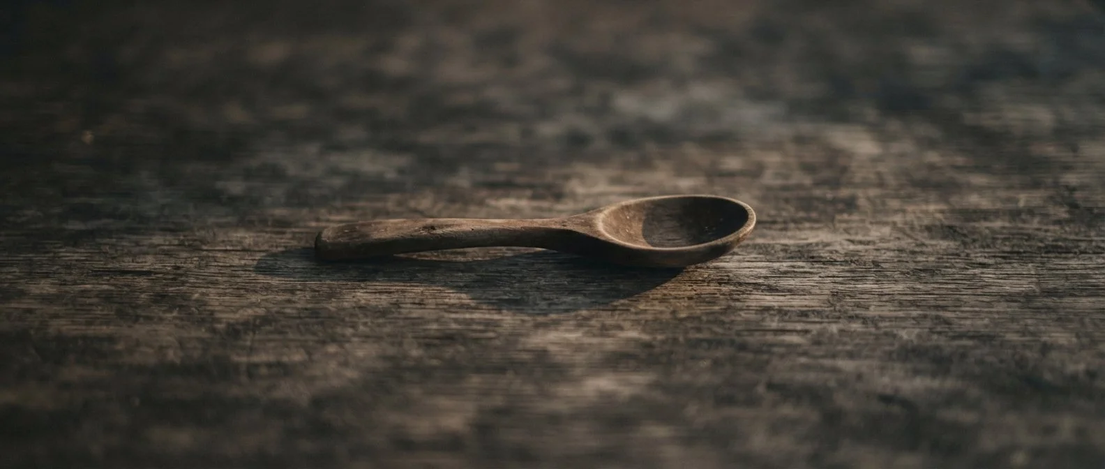 A small wooden spoon lying on a weathered wooden surface.