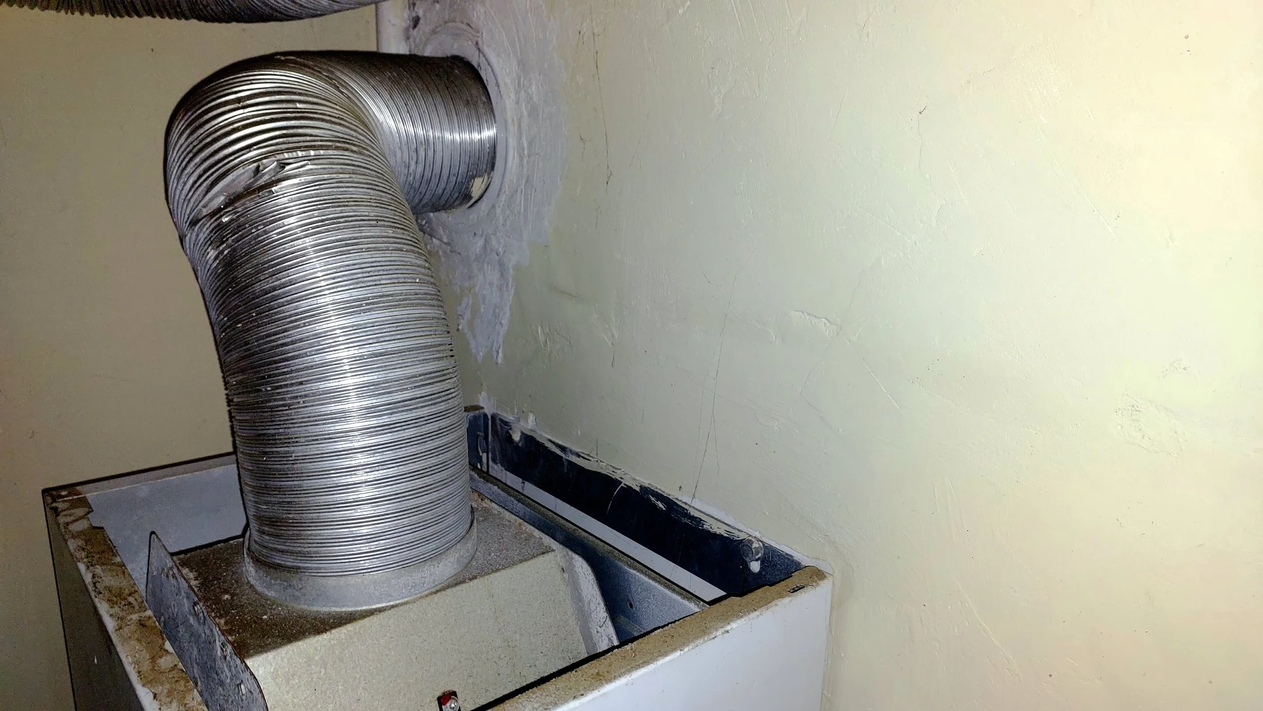 A kitchen range with a damaged and discolored stovetop, a metal ventilation duct, and a wall with peeling paint and cracks.