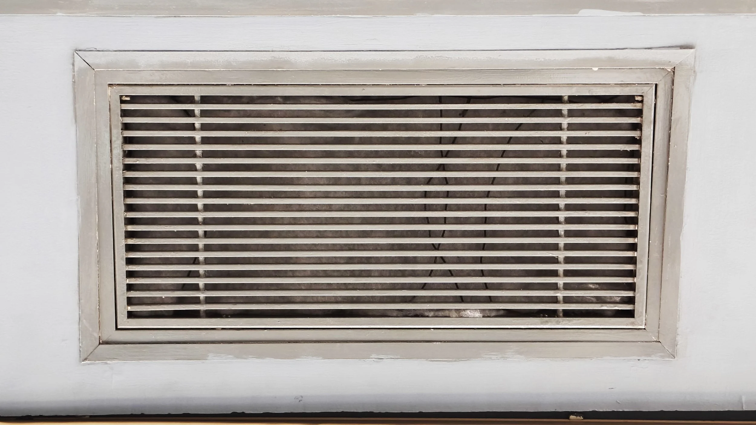 A ceiling air vent cover with horizontal slats, framed by a white ceiling and wall.