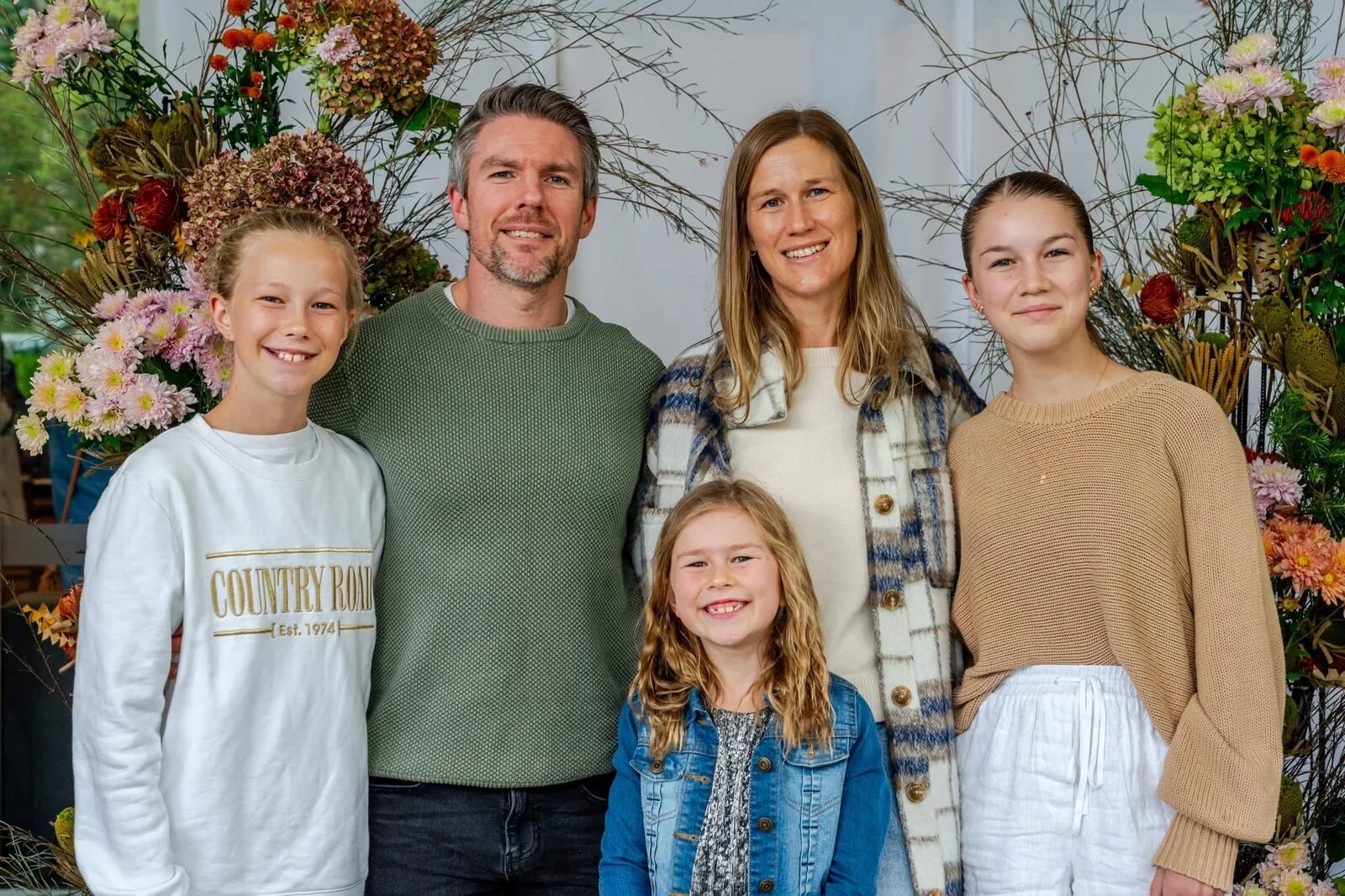 Phil and Lozzie Rawnsley with their three daughters, Team Rawnsley, smiling together in front of a floral display.