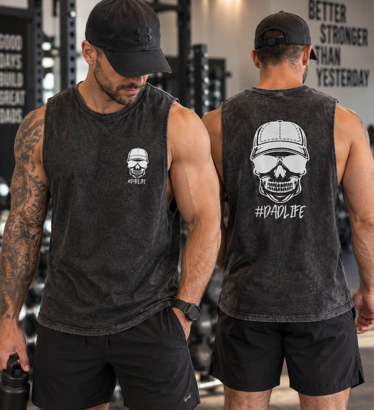 Two muscular men wearing black sleeveless shirts and black baseball caps standing in a gym, both showing a skull and cap logo on their shirts with the hashtag #DADLIFE, surrounded by gym equipment and motivational wall art.