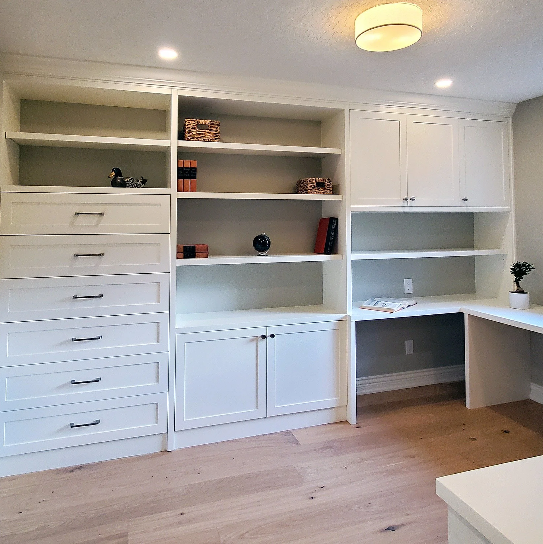 White built-in home office with integrated desk, open shelving, drawers and concealed storage.
