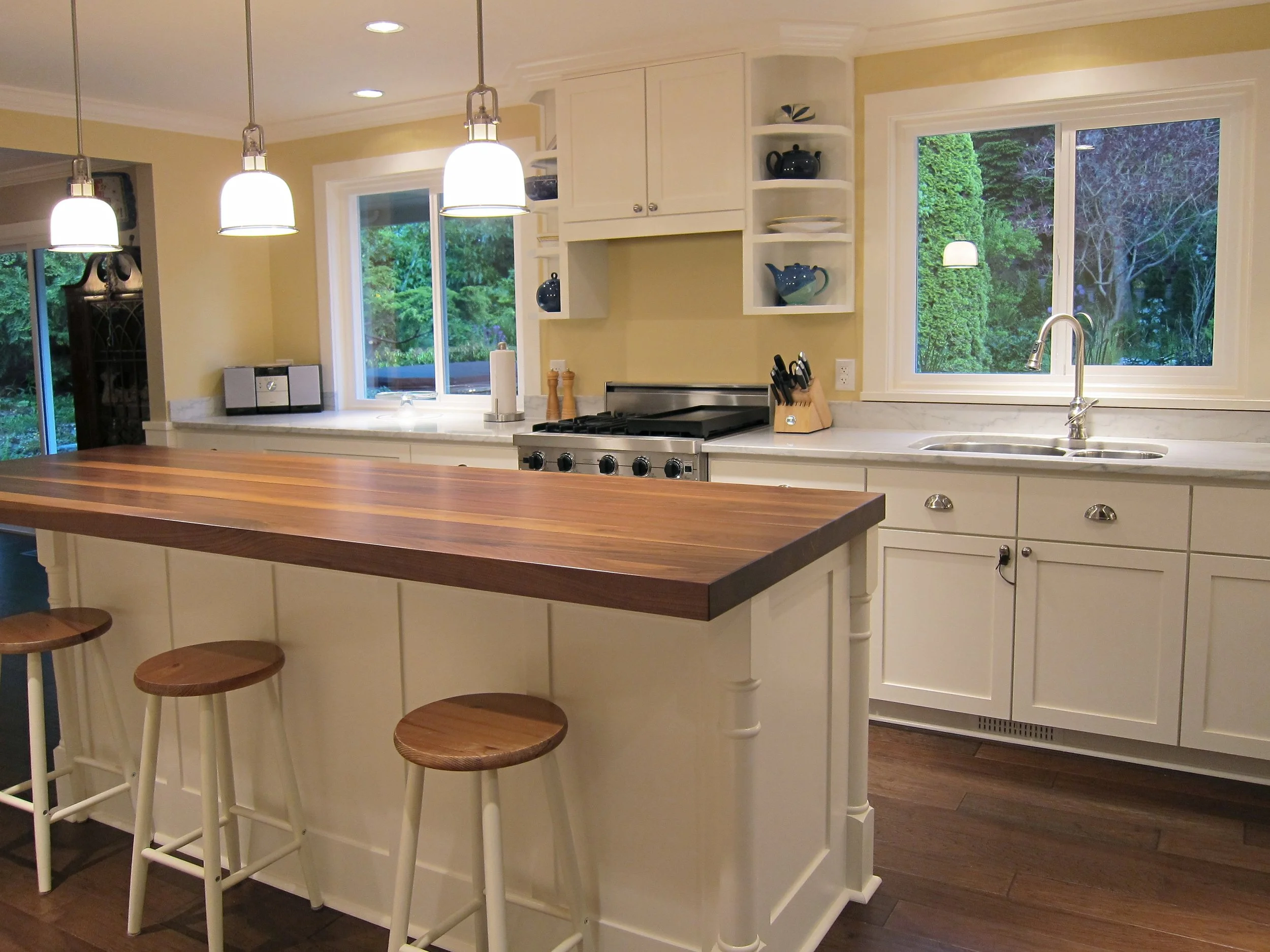 Cream kitchen with a generous wood-topped island, pendant lighting and garden-facing windows.