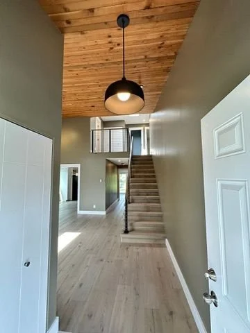 Interior view of a house entryway with a staircase leading to the second floor, wood ceiling, and hanging ceiling light.
