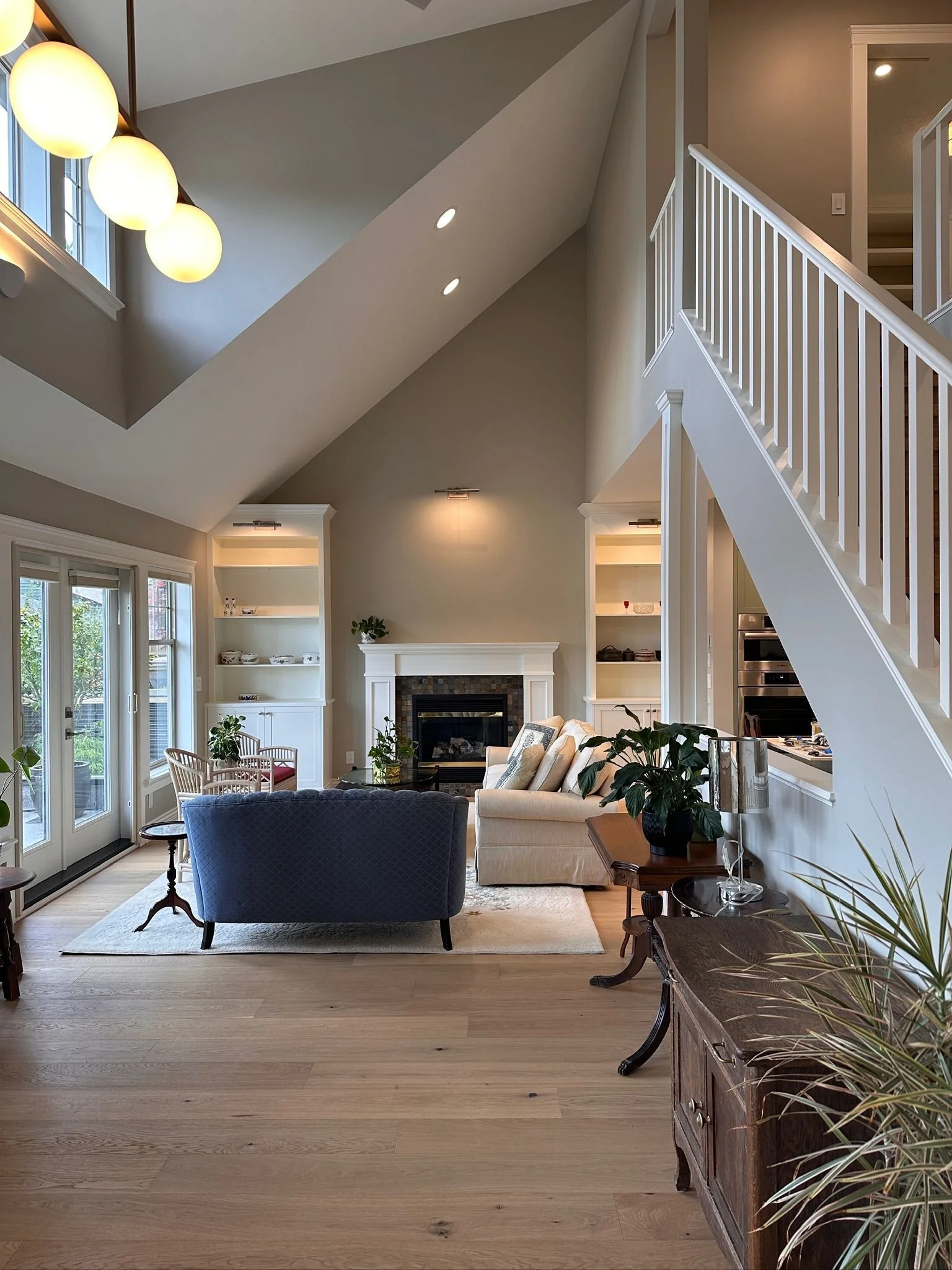 Living room with high vaulted ceiling, large windows, a fireplace, and seating including a beige sofa and blue armchair.