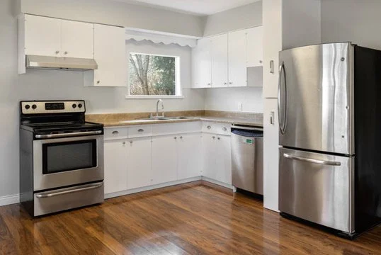 Kitchen with white cabinets, stainless steel refrigerator, stove, dishwasher, and wooden floor.