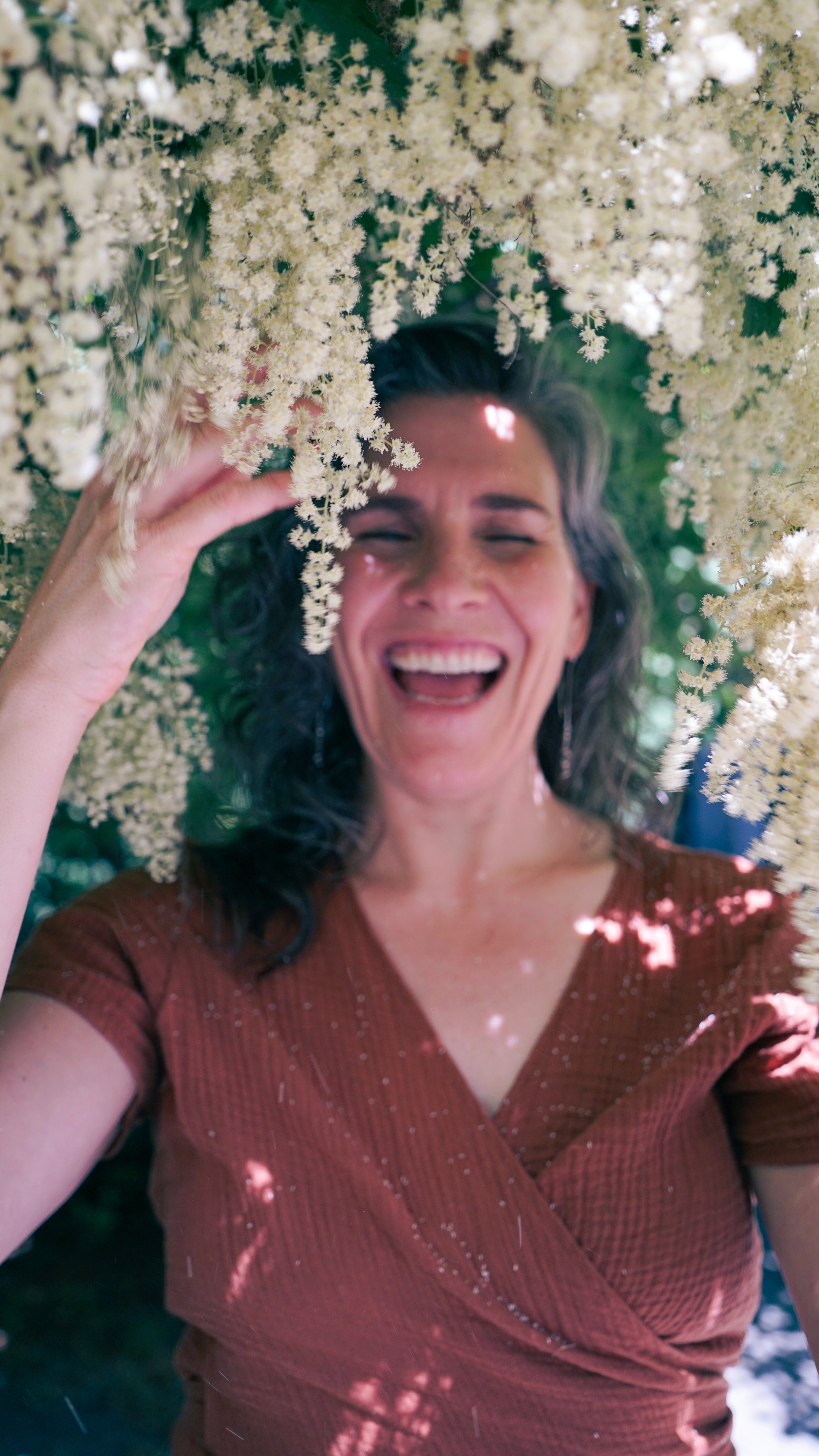 Photo of Robin with eyes closed laughing in a bush of ocean spray flowers