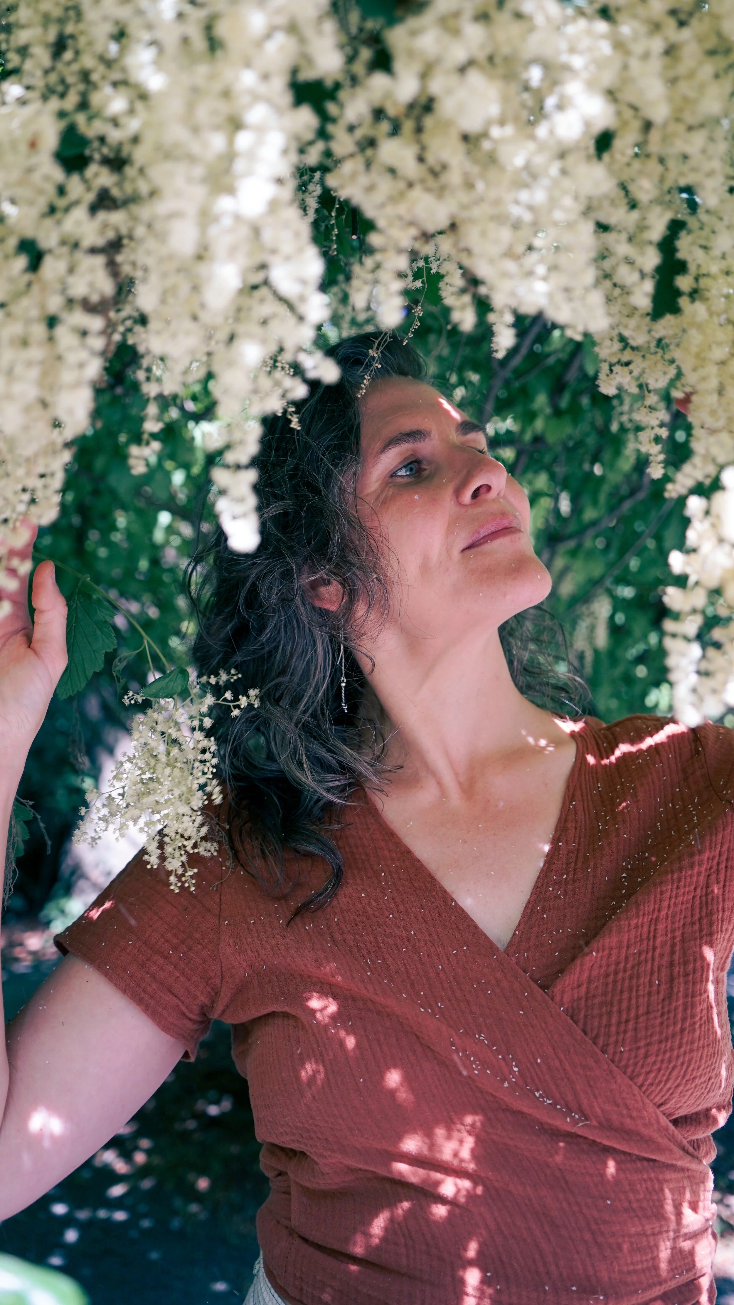 Robin gazing up at flowering ocean spray white flowers with a soft smile on her face
