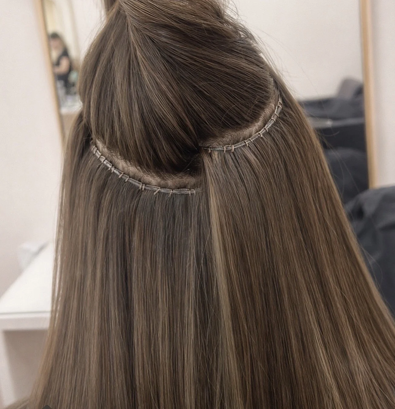 Hair extensions attached to a person's hair in a salon, with the extension wefts sewn into the natural hair.