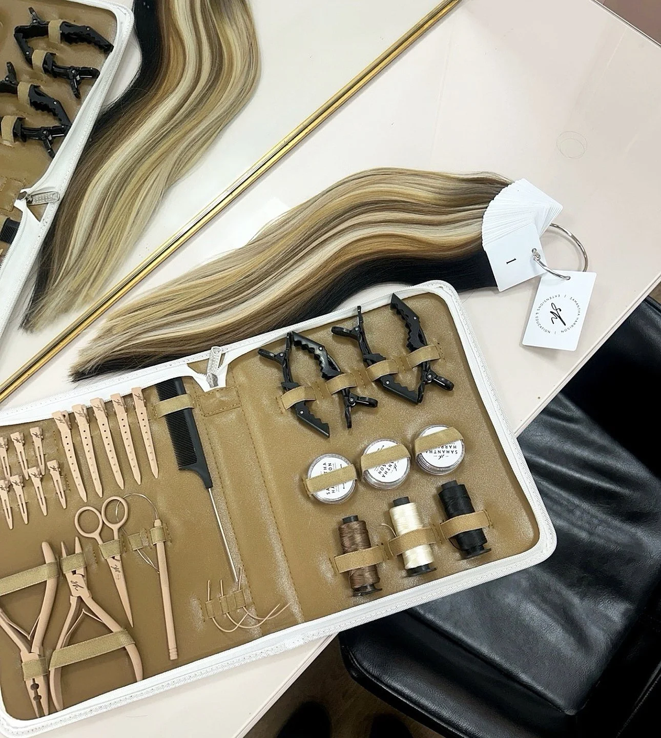 Hair extension toolkit with hair strands, clips, small containers, scissors, and combs arranged on a beige mat inside a white case.