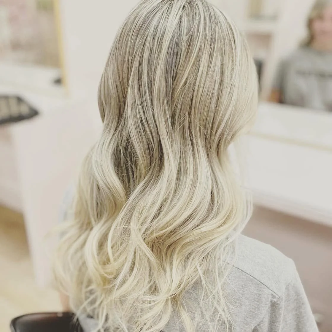 Back view of a woman with long, wavy, platinum blonde hair in a salon.