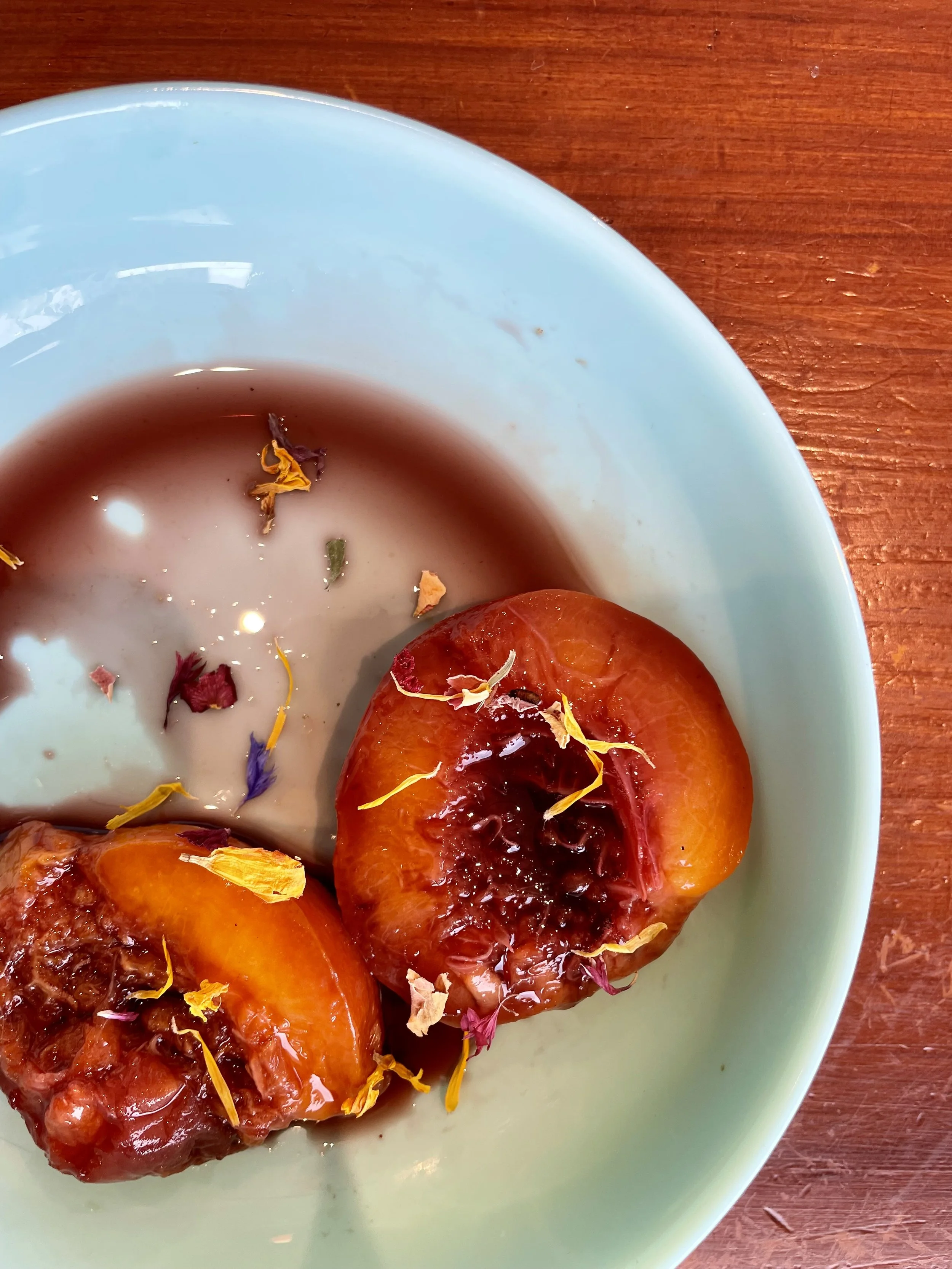 Prune fraîche garnie de sirop et de fleurs comestibles dans une assiette bleue sur une table en bois.