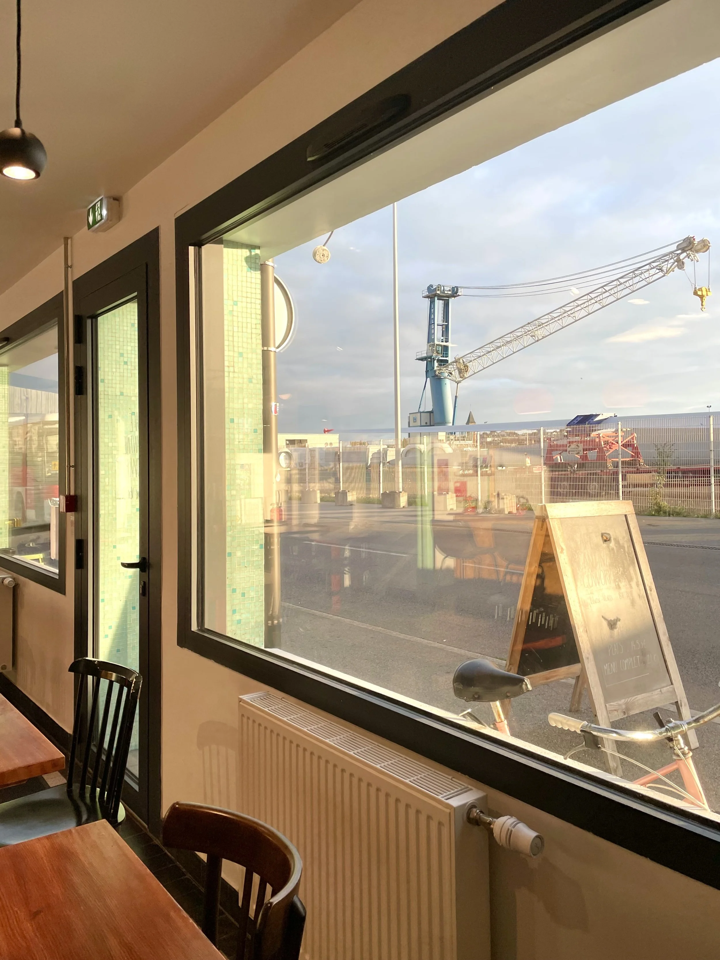 Vue depuis l'intérieur d'un café ou restaurant vers la fenêtre, montrant un chantier avec une grue en plein travail à l'extérieur.