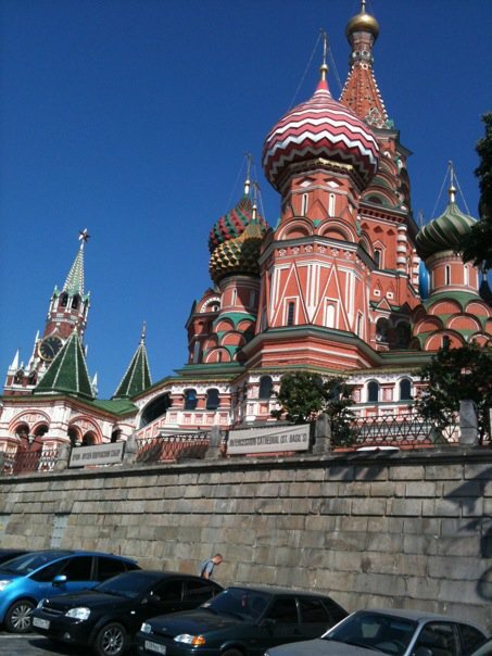 St. Basil's Cathedral in Moscow with colorful onion domes and a stone wall in the foreground, under a clear blue sky.
