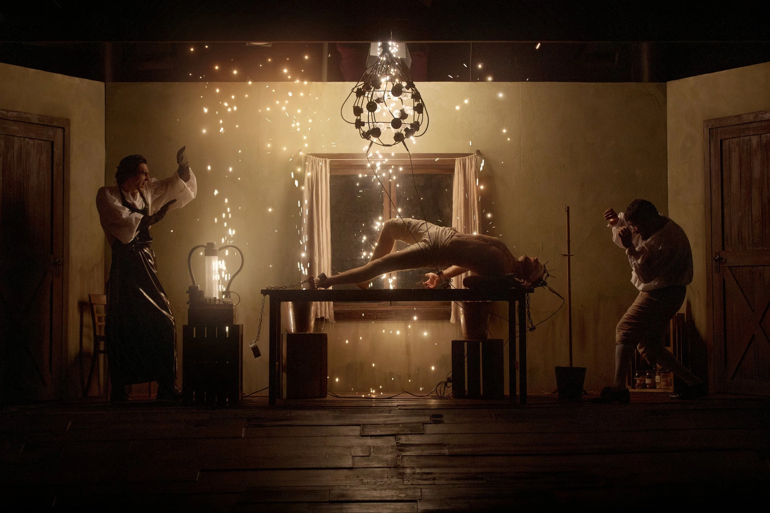 Scene from 'Frankenstein' showing the reanimation of Frankenstein's Monster. Sparks and light effects fill the room, creating a spooky and theatrical atmosphere.
