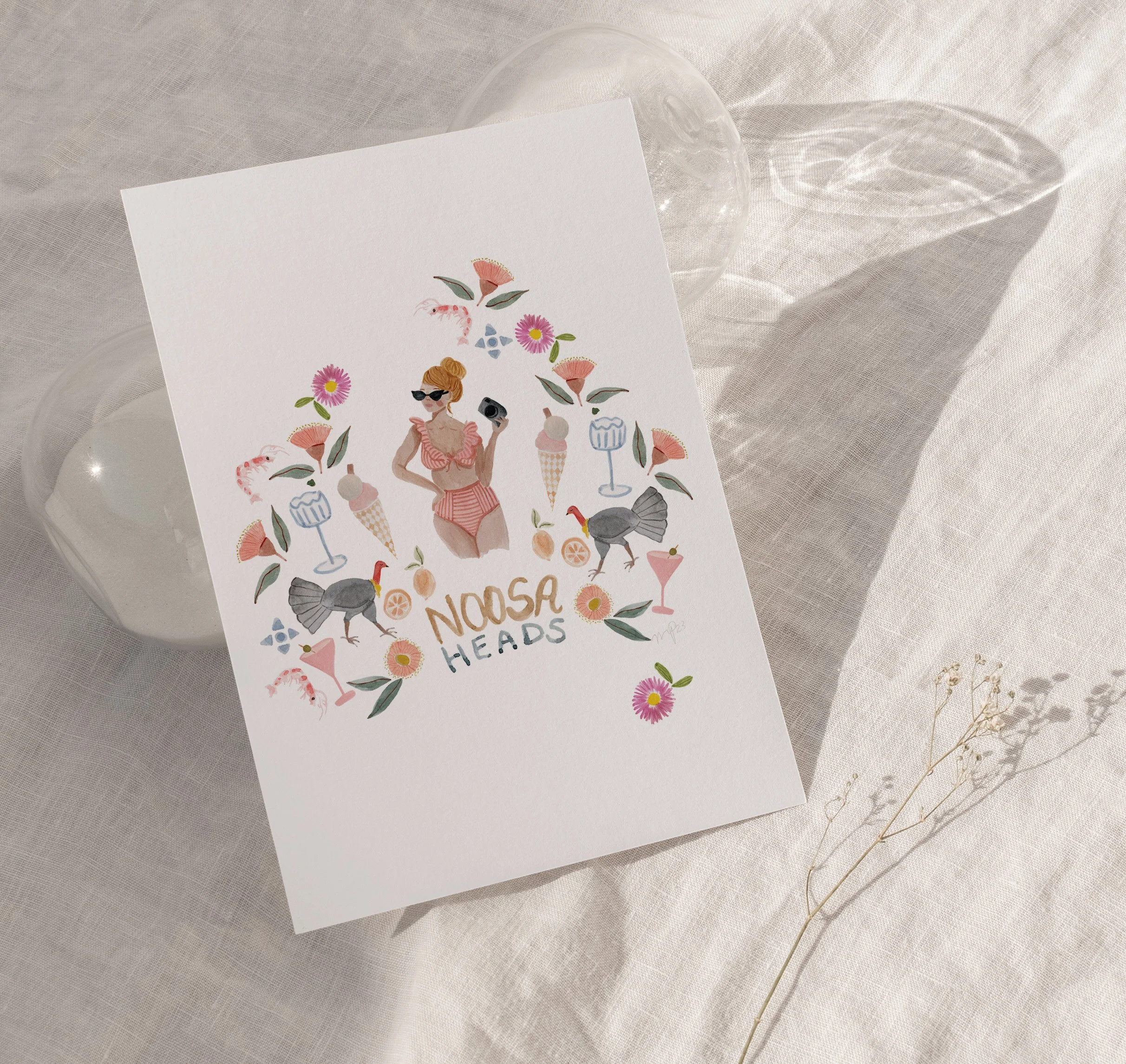 A white card with colorful illustrations of a woman in sunglasses, flowers, ice cream, and turkey on a table with a transparent glass plate and a beige tablecloth.