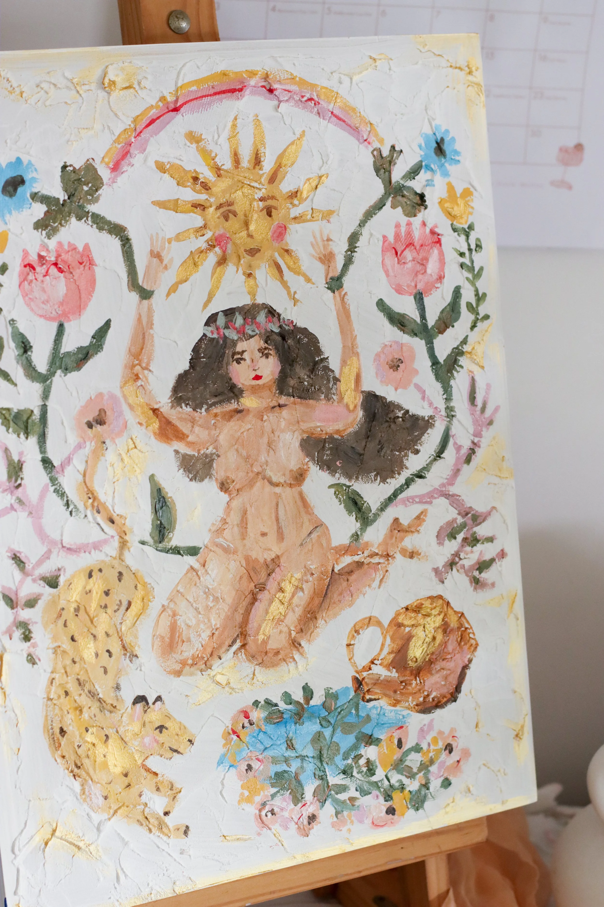 A colorful painting depicting a nude woman with dark curly hair sitting surrounded by flowers, a sun with a face, and a rainbow, with a textured background.