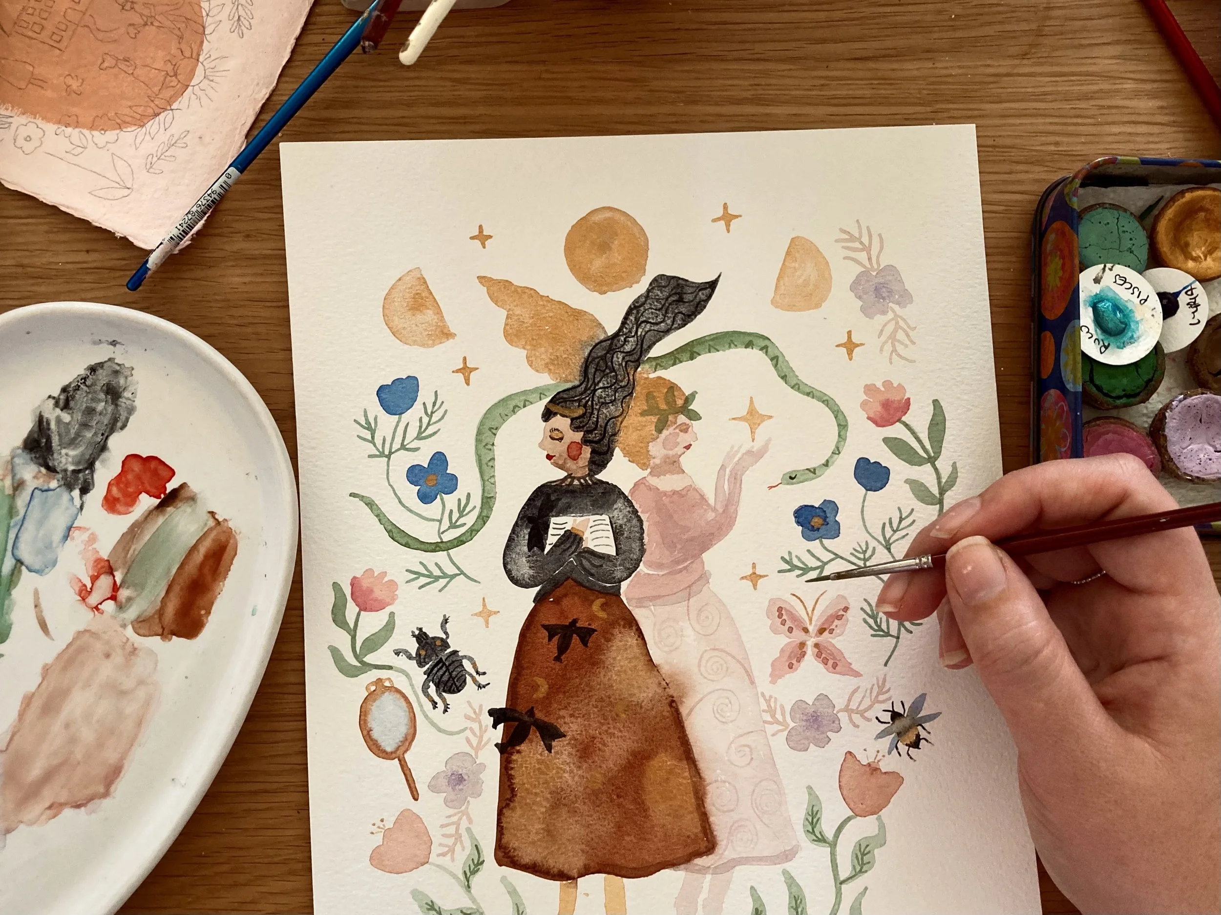 A watercolor painting of a woman with long curly black hair, holding a book, surrounded by plants, flowers, moons, stars, and insects, with earthy tones and a whimsical style.