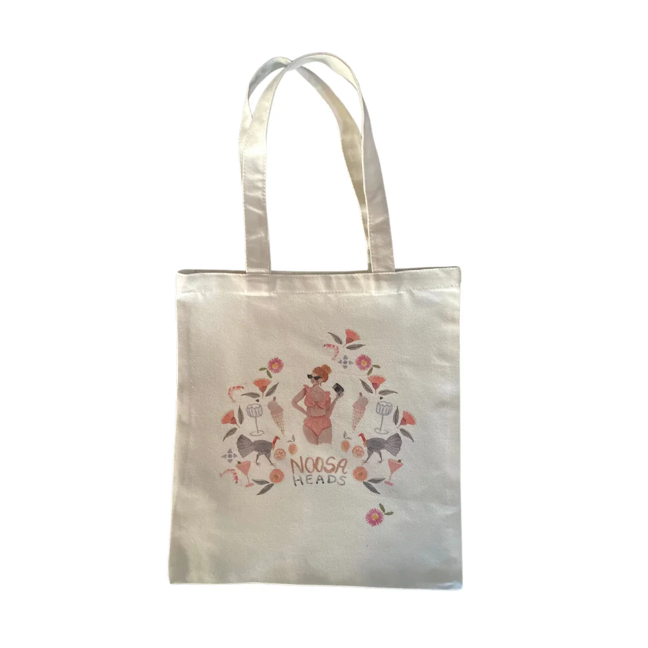 White tote bag with a printed design of a woman wearing sunglasses surrounded by flowers, birds, and drink glasses, with the text 'NOOSA HEADS' at the bottom.
