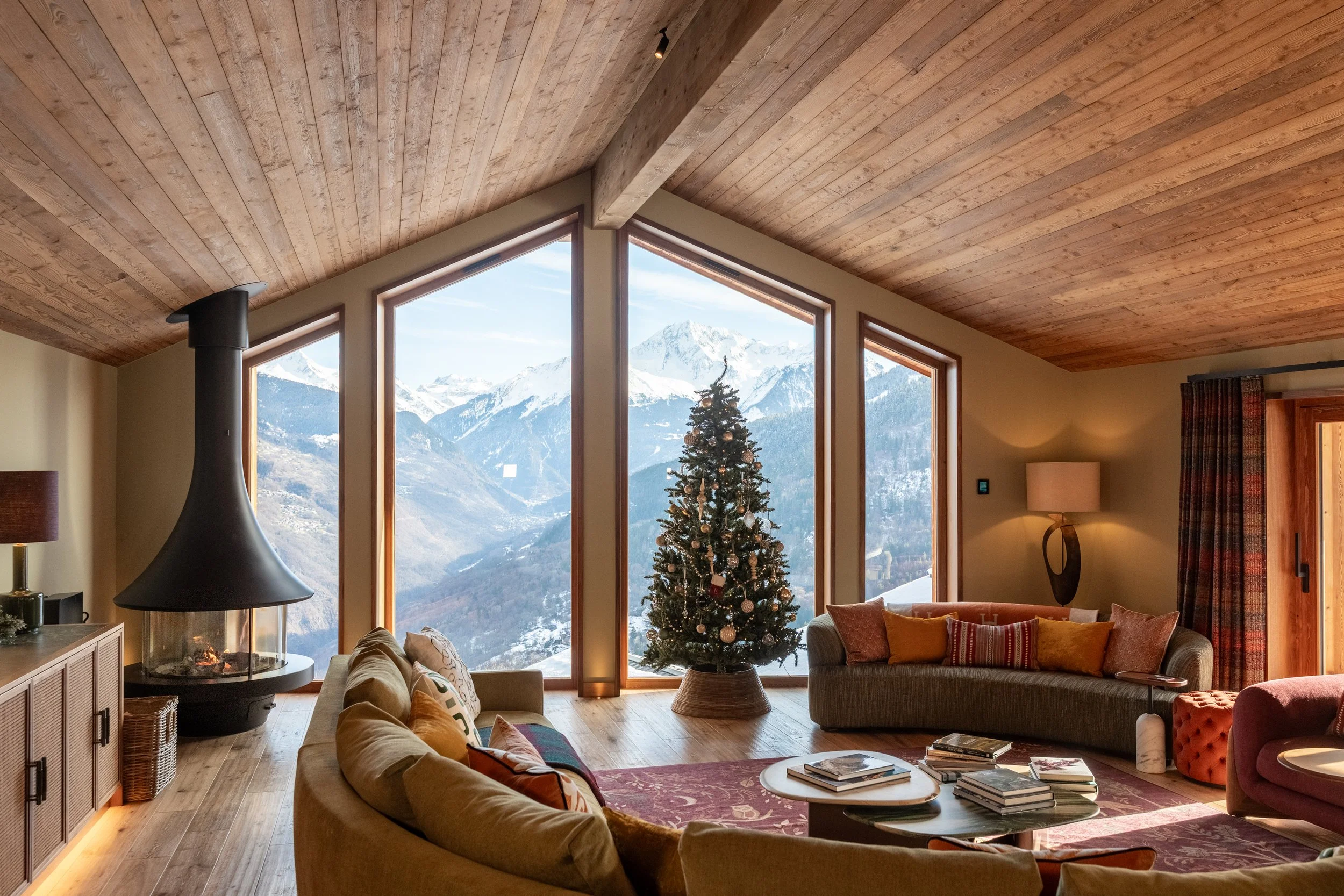 Cozy Chalet Springfield living room with a decorated Christmas tree, modern fireplace, wood-paneled ceiling, and panoramic snowy mountain views