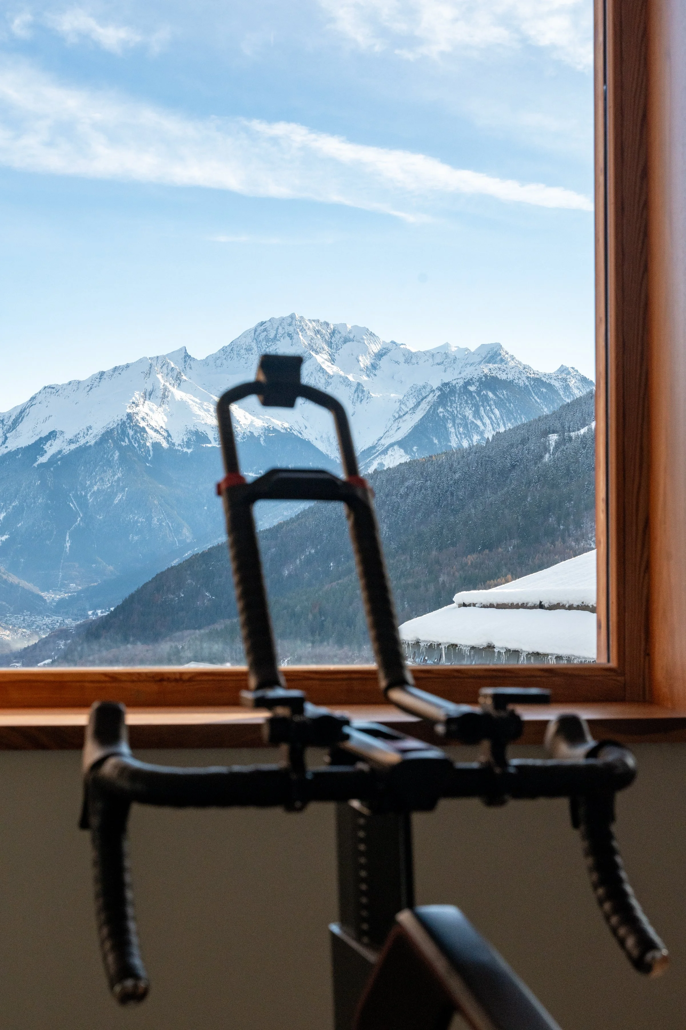 Snow-covered mountain range viewed through a wooden window, with a ski rack in the foreground.