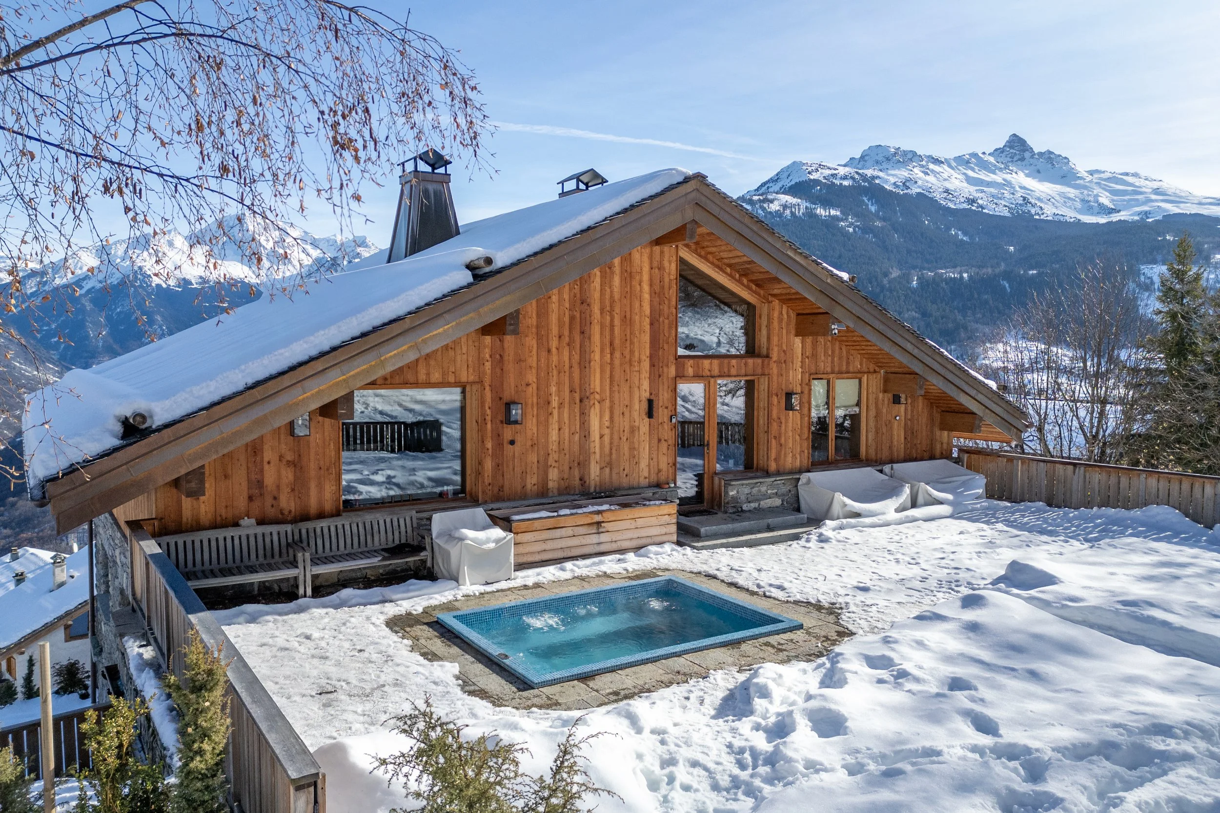 Snow-covered wooden mountain chalet with outdoor pool and alpine peaks in the background